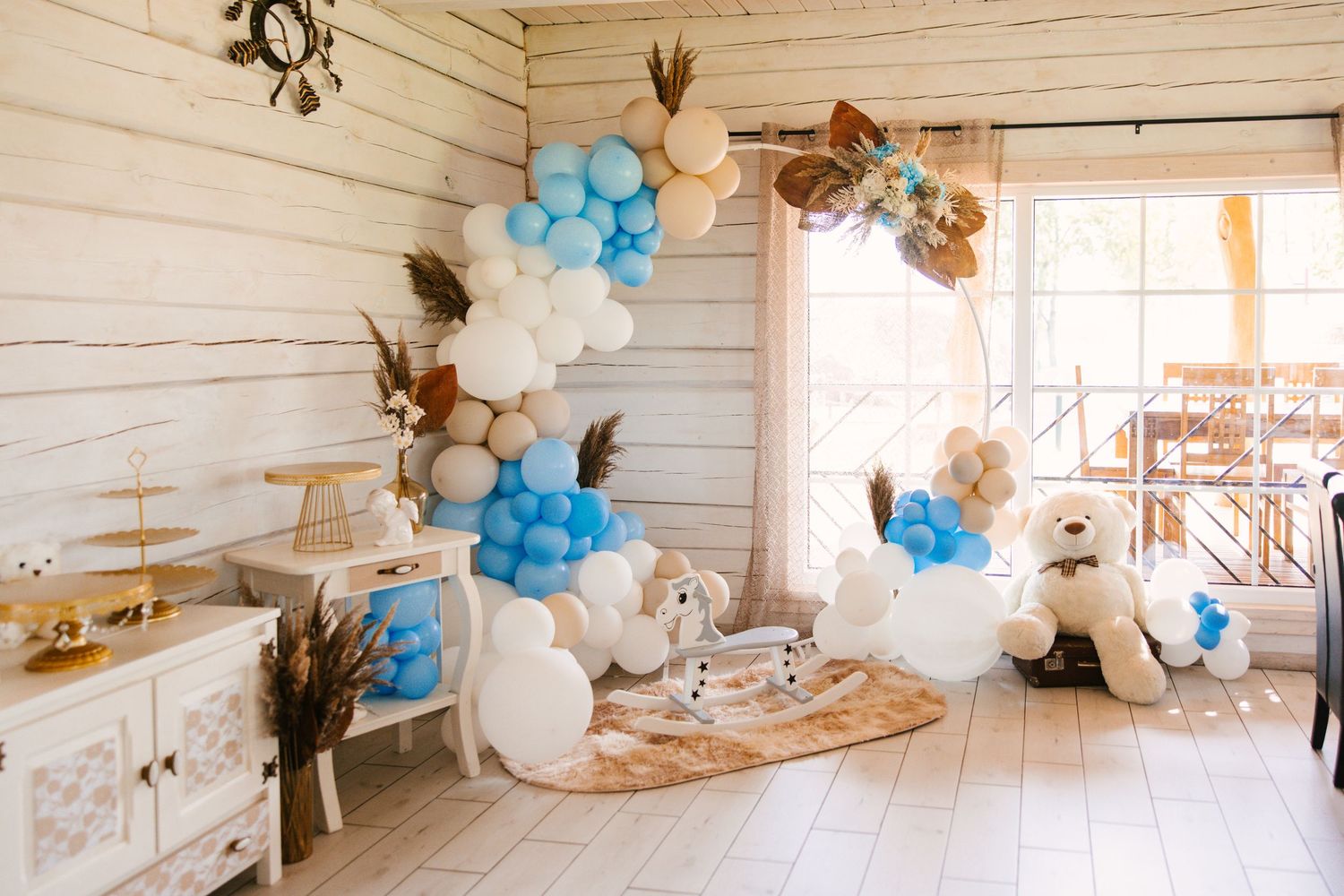 Rustic baby shower setup with blue and white balloon garlands in a wooden room.