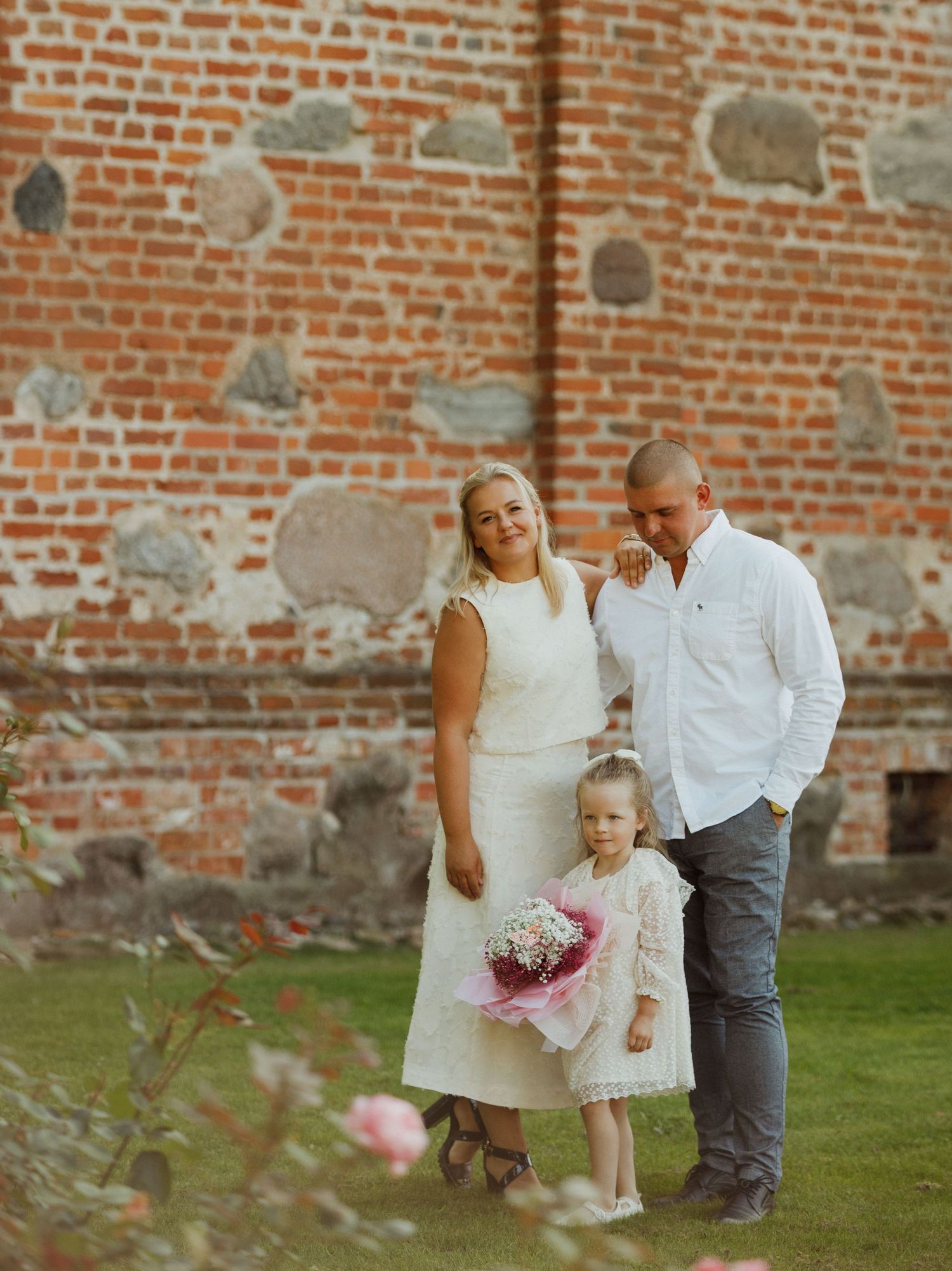 Family captures sweet moments together against rustic brick wall in garden setting.