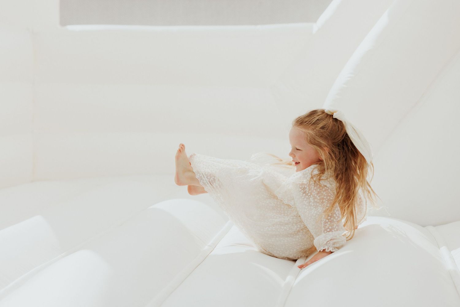Child playing and stretching on white bouncy surface with joyful expression.