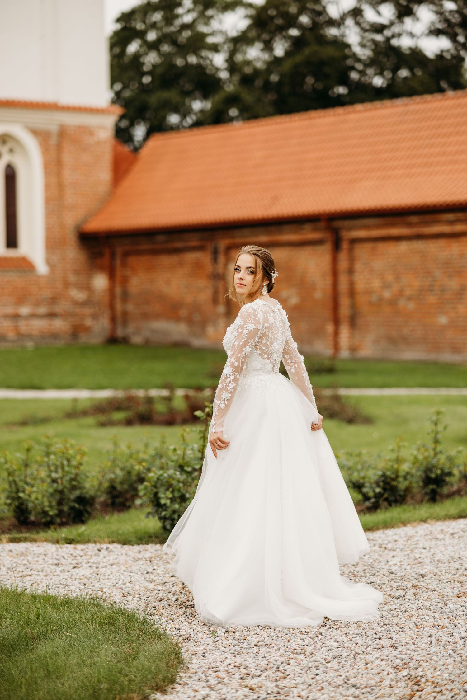 White wedding dress on gravel path with brick church architecture in background.