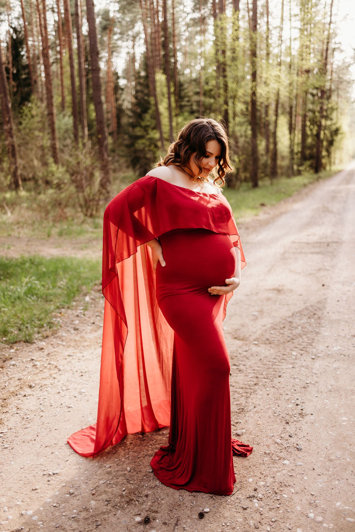 Artistic maternity photography series featuring a flowing red dress on a forest trail.