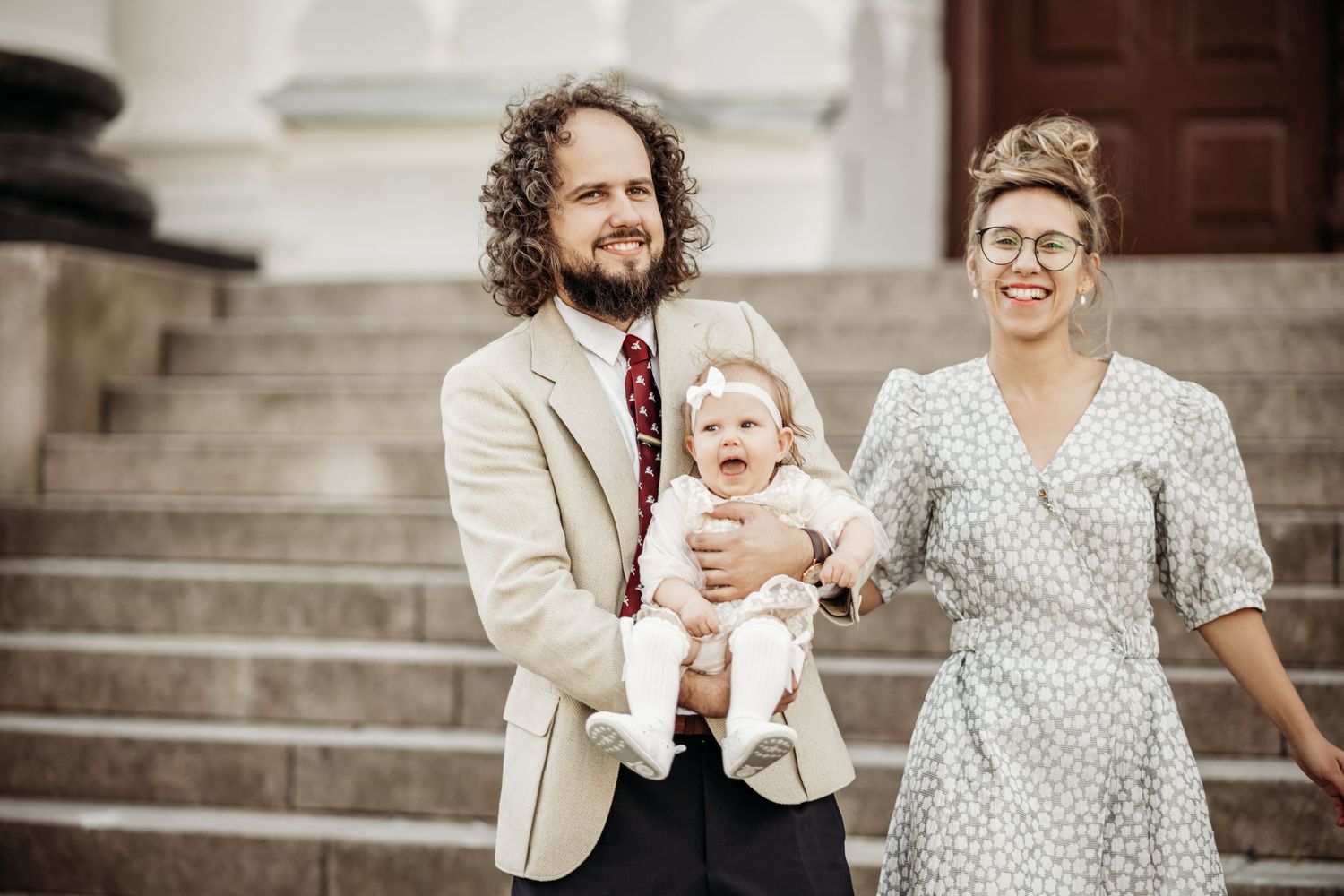 A couple and their baby pose on stone steps during a formal family photo session.