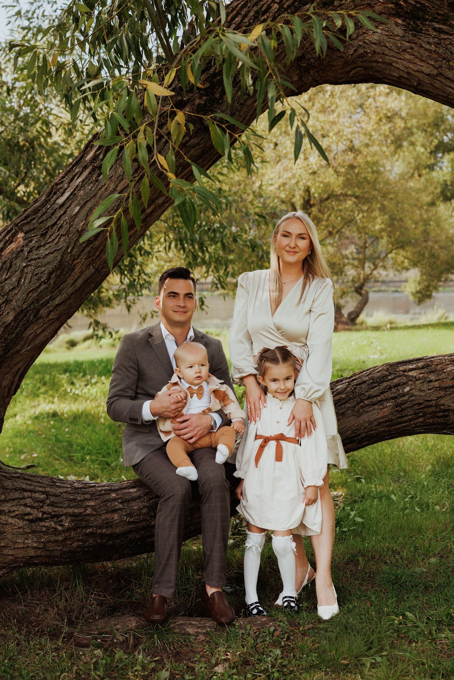 A family poses together under a large tree branch in an outdoor setting wearing coordinated formal attire.