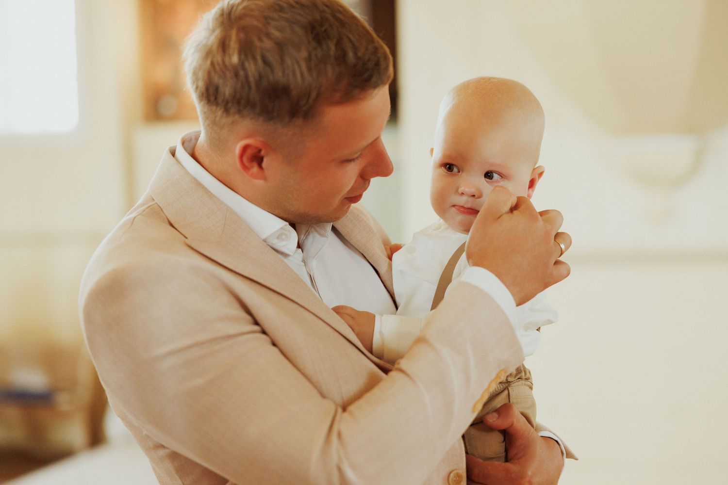 A tender moment between parent and baby in white clothing against a warm indoor setting.