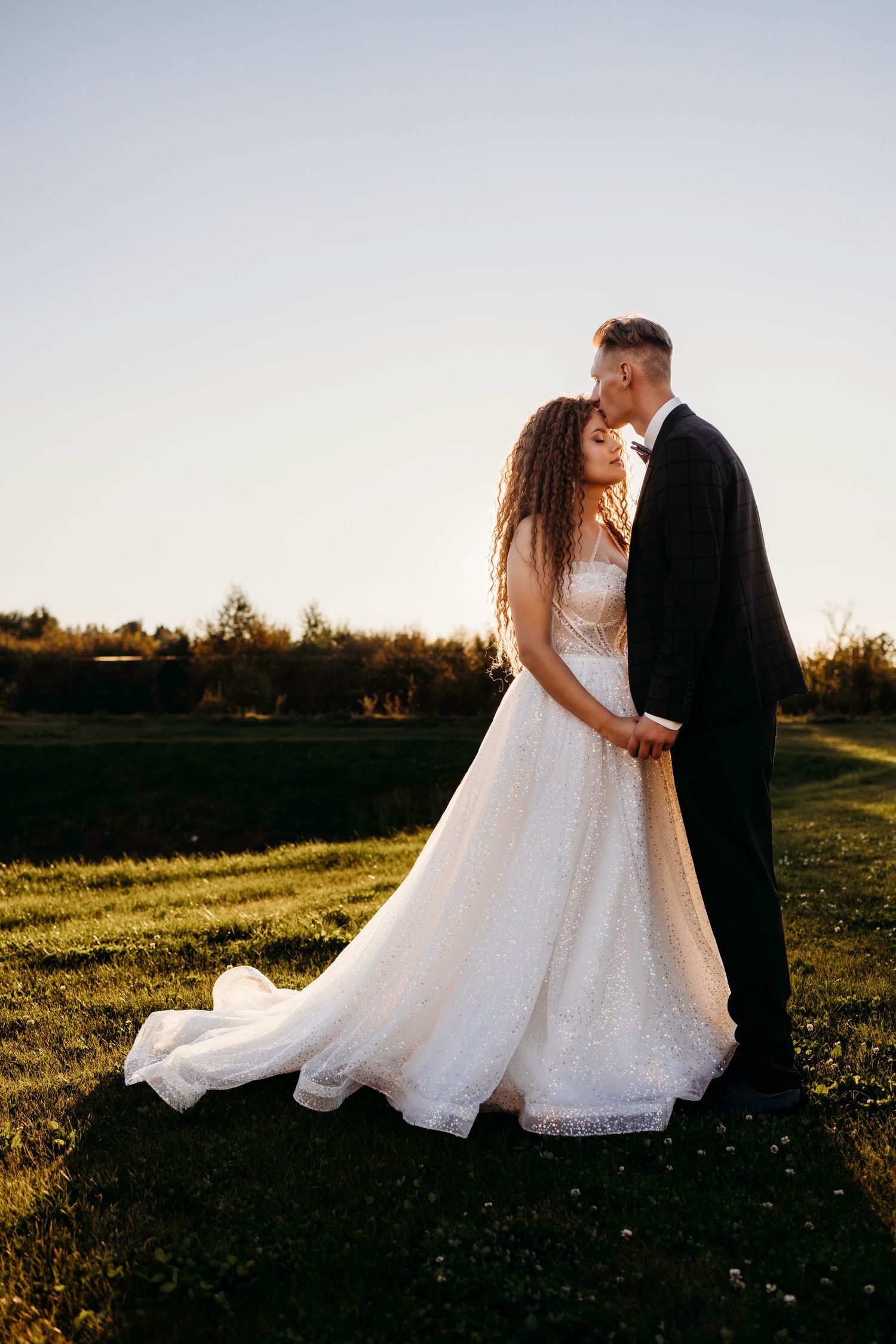 Romantic sunset wedding photos of couple in white dress and black suit in a golden meadow.