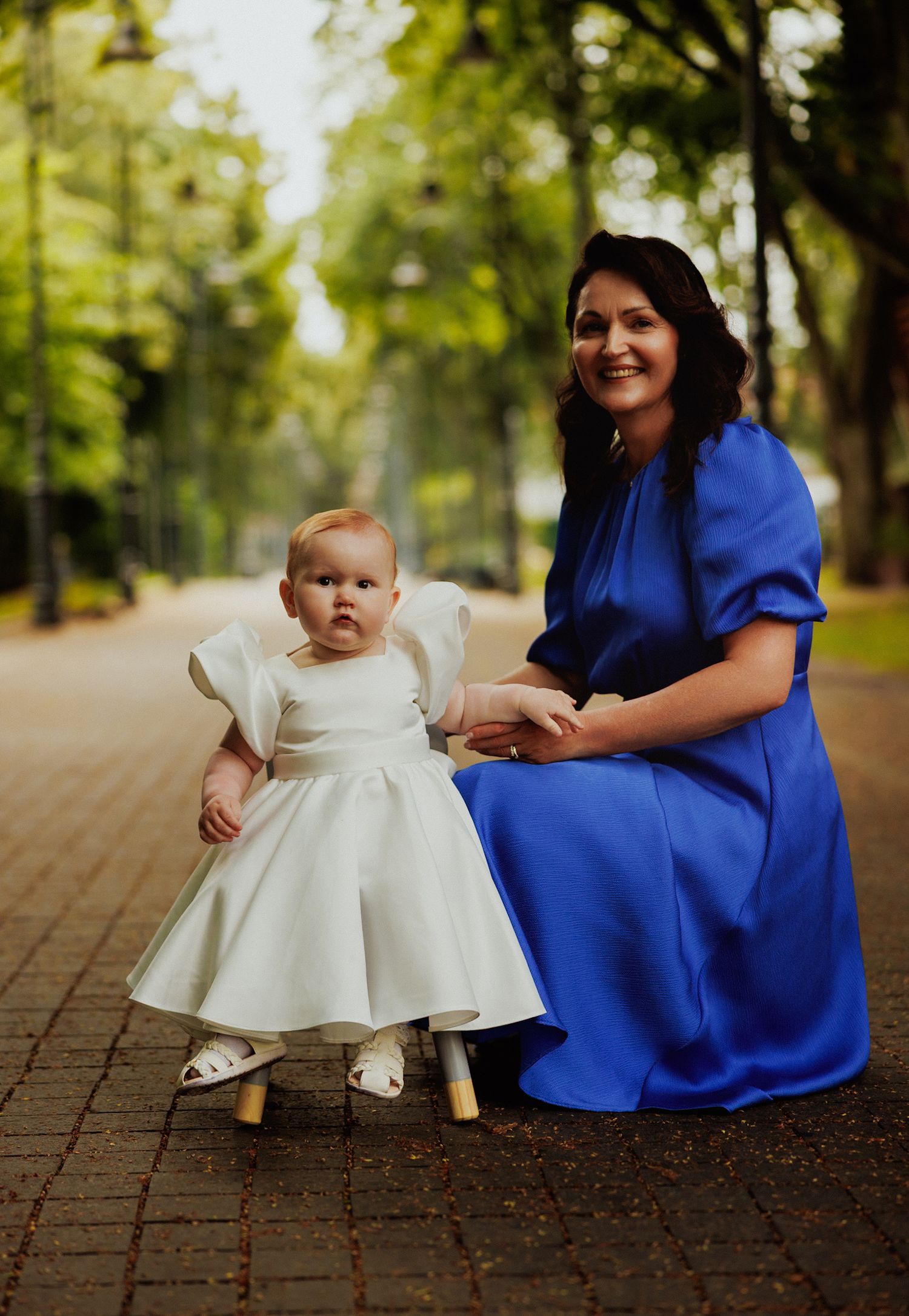 A series of intimate portraits showing a small child in white dress sitting beside someone in royal blue on brick pavement.