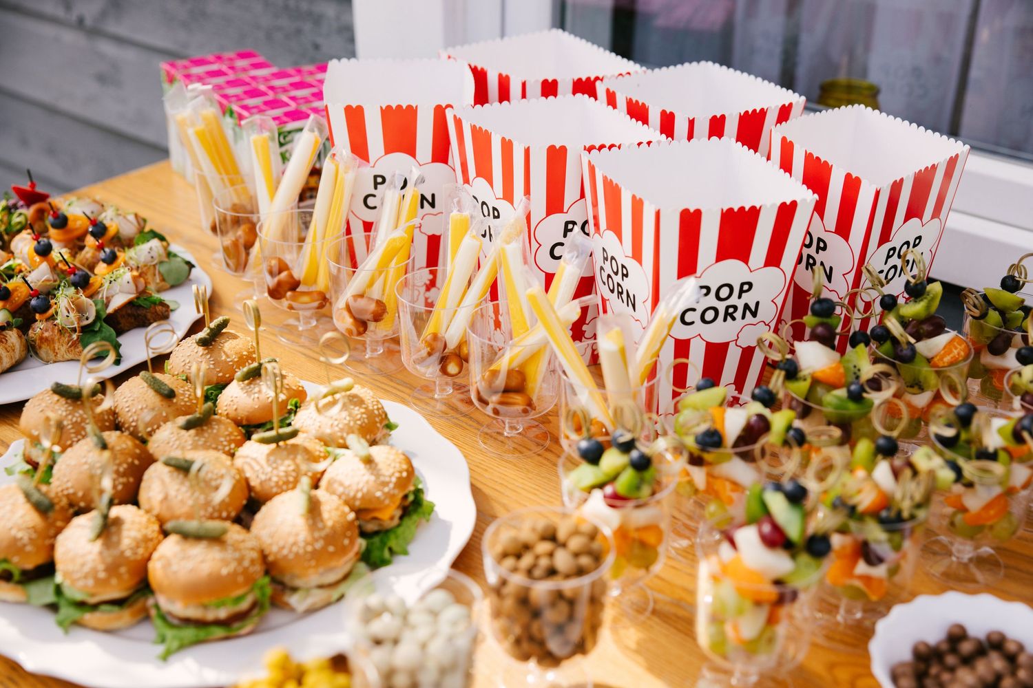 Party food spread featuring mini burgers, popcorn, and appetizers on a buffet table.