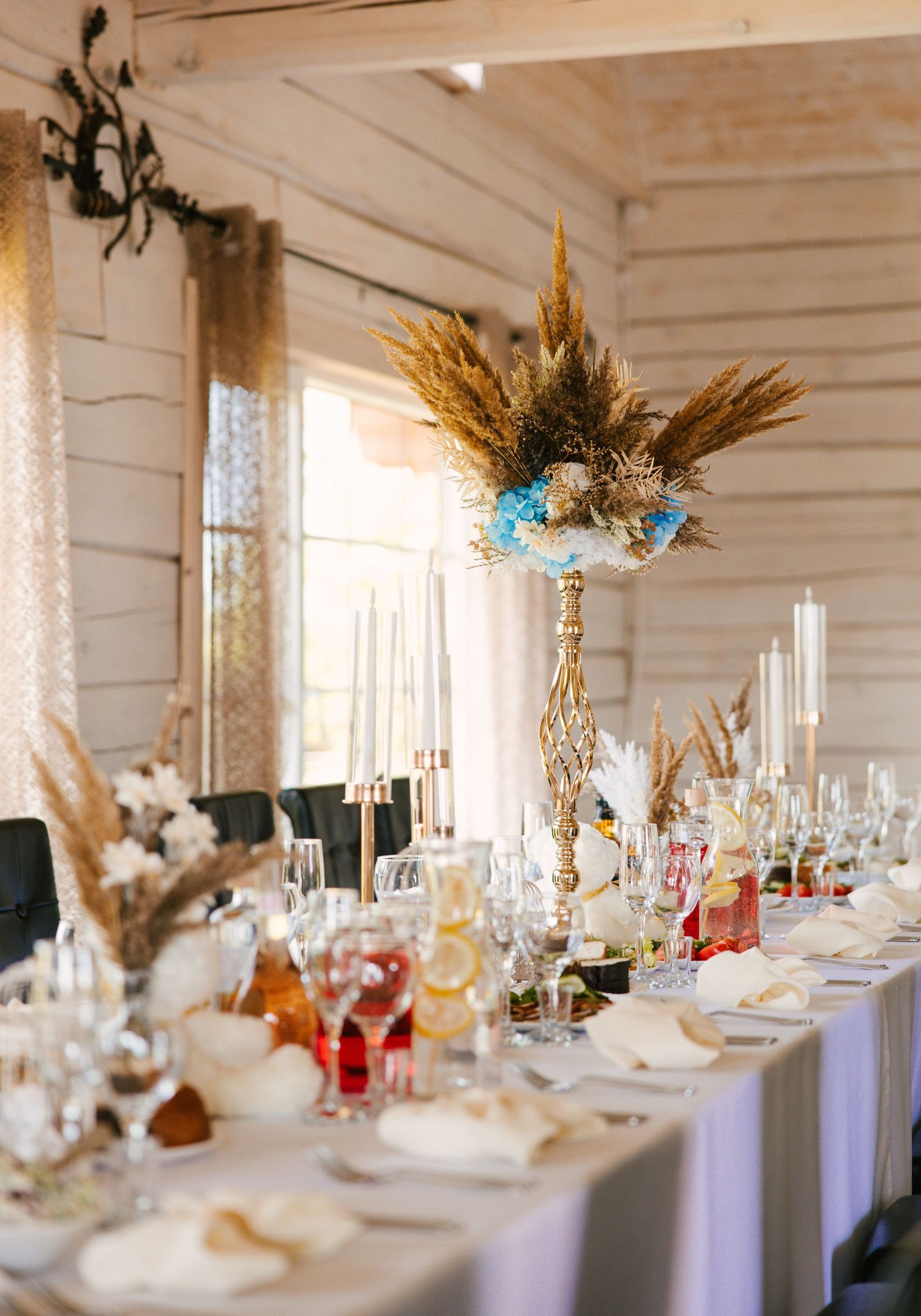 Long dining table with golden vases filled with pampas grass and blue flowers.