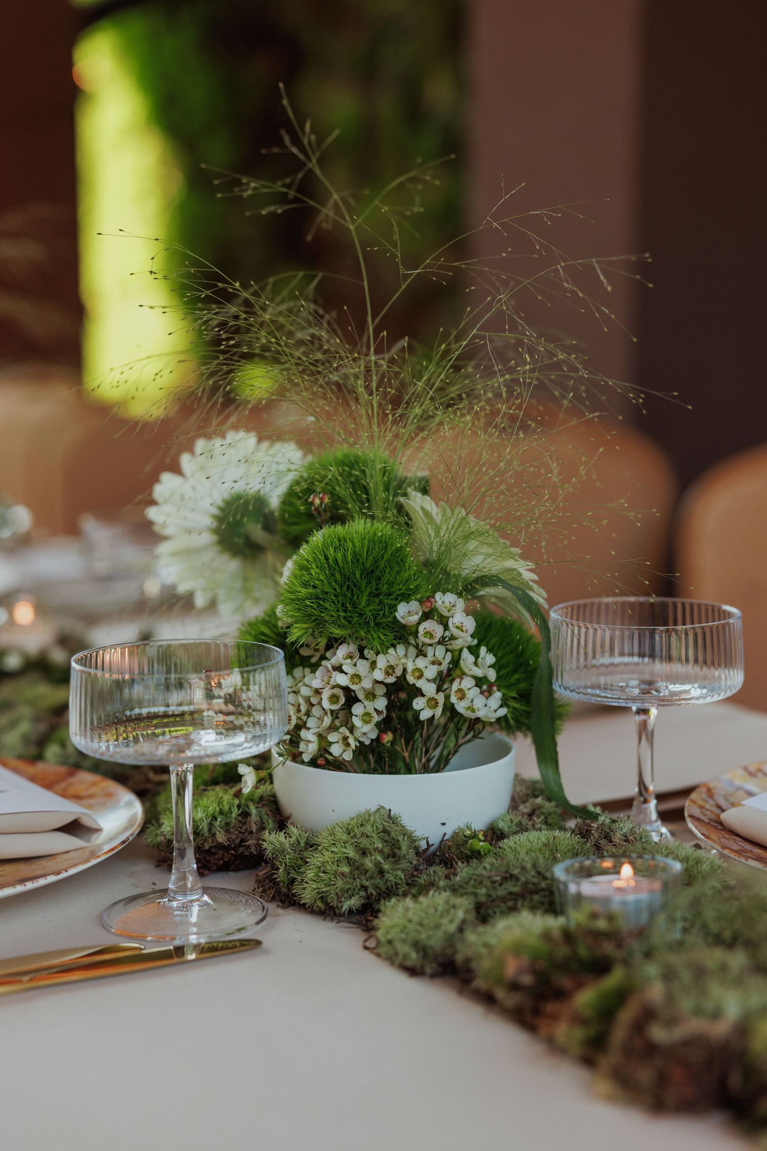 Romantic table setting with green moss centerpieces, delicate glassware, and soft candlelight.