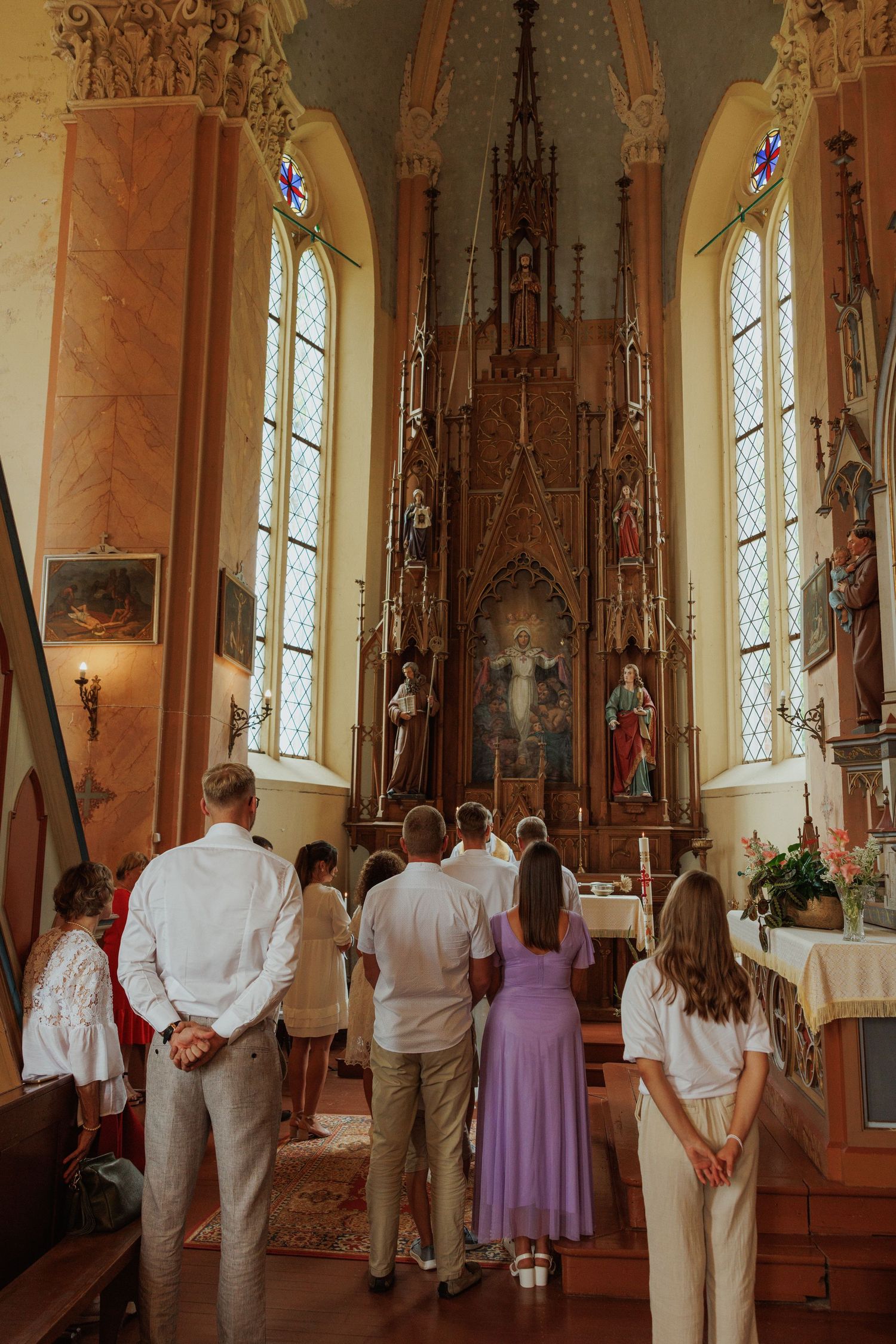 Wedding guests gather in a traditional church with gothic architecture and stained glass windows.