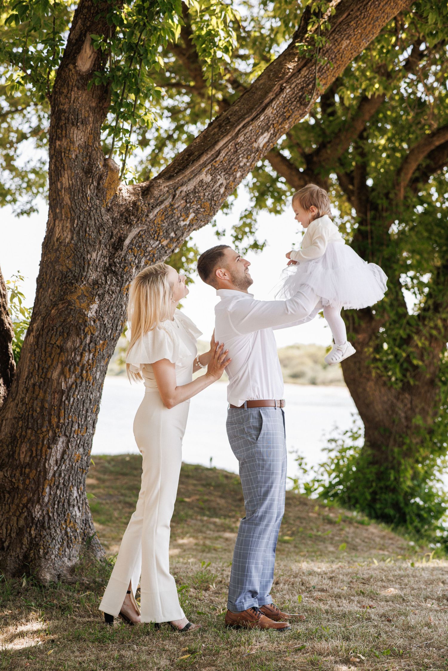 A couple in white and blue attire dances together under large trees in a romantic outdoor setting.