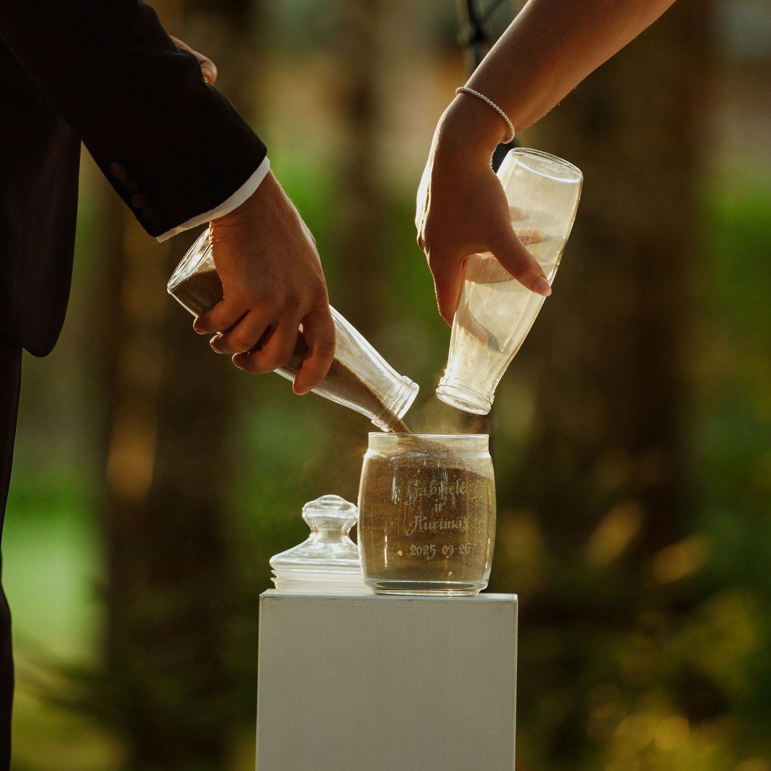 Hands placing or arranging glass containers on white pedestals at outdoor event.