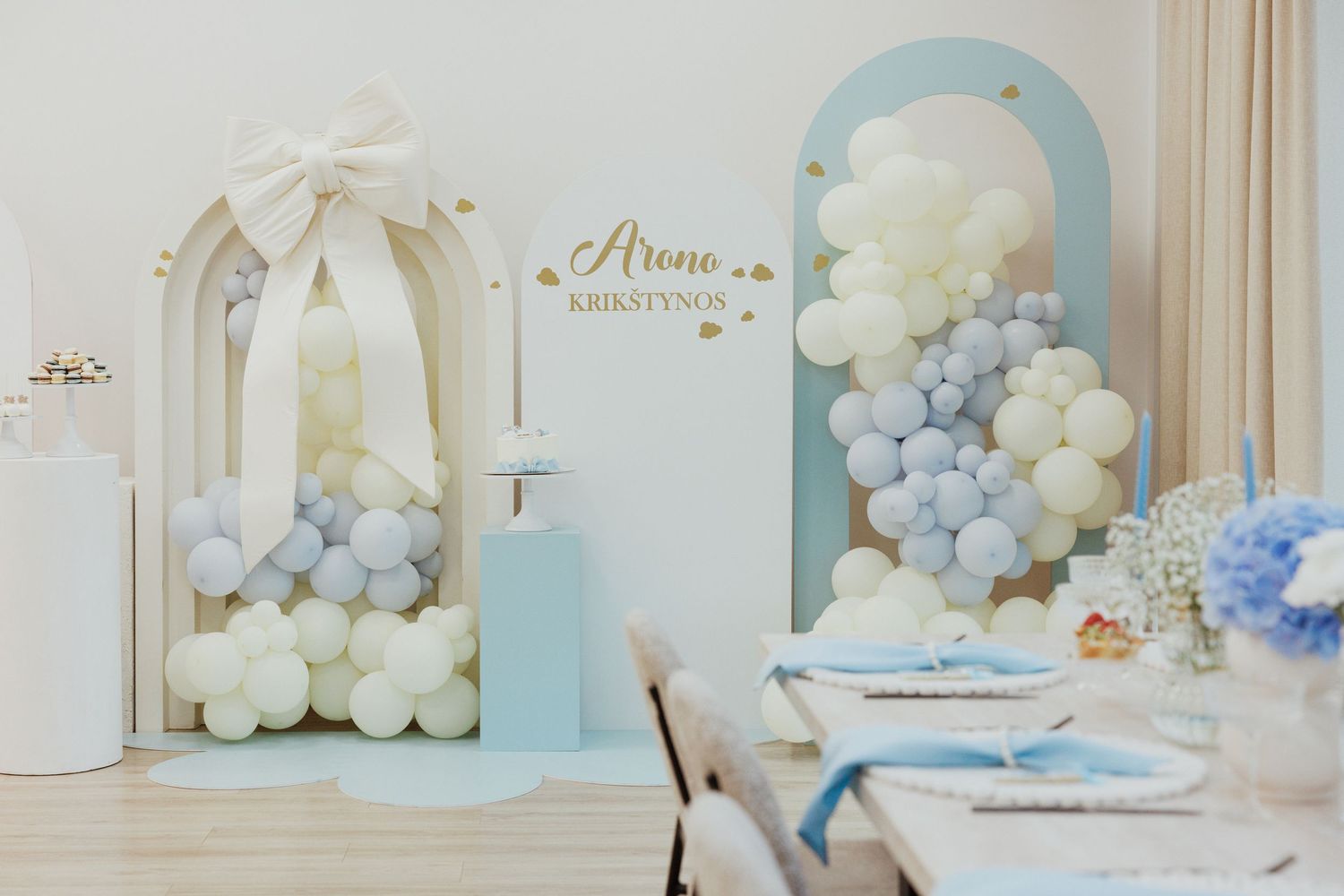 Elegant party setup with white and blue balloon garlands and table decorations.