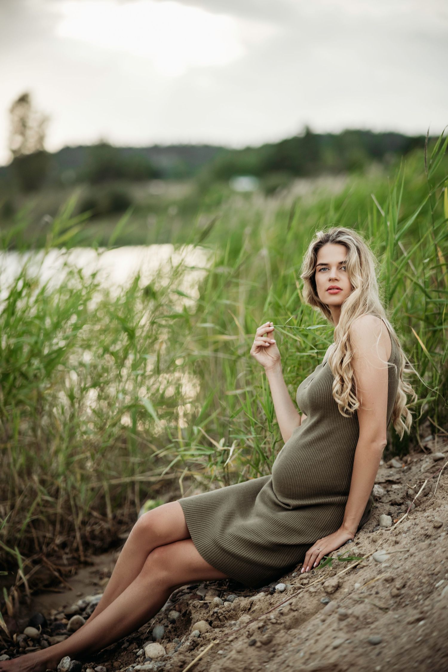 Maternity portraits in an olive dress amid tall grass and natural scenery.