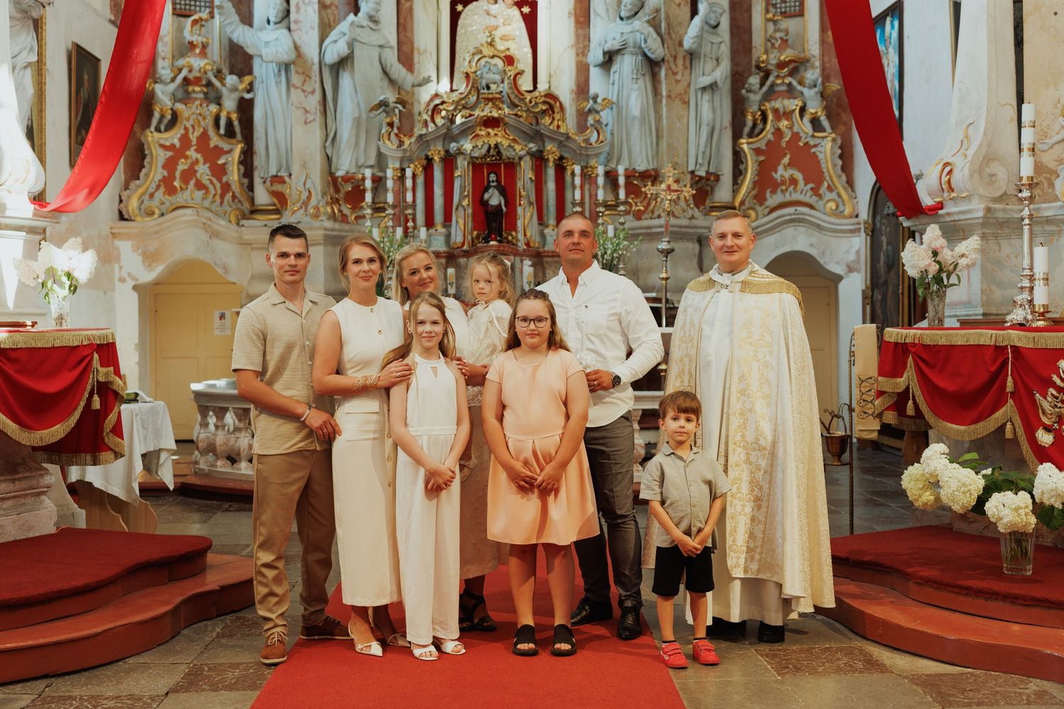 Children in white and peach formal attire stand together during a special ceremony in an ornate church setting.