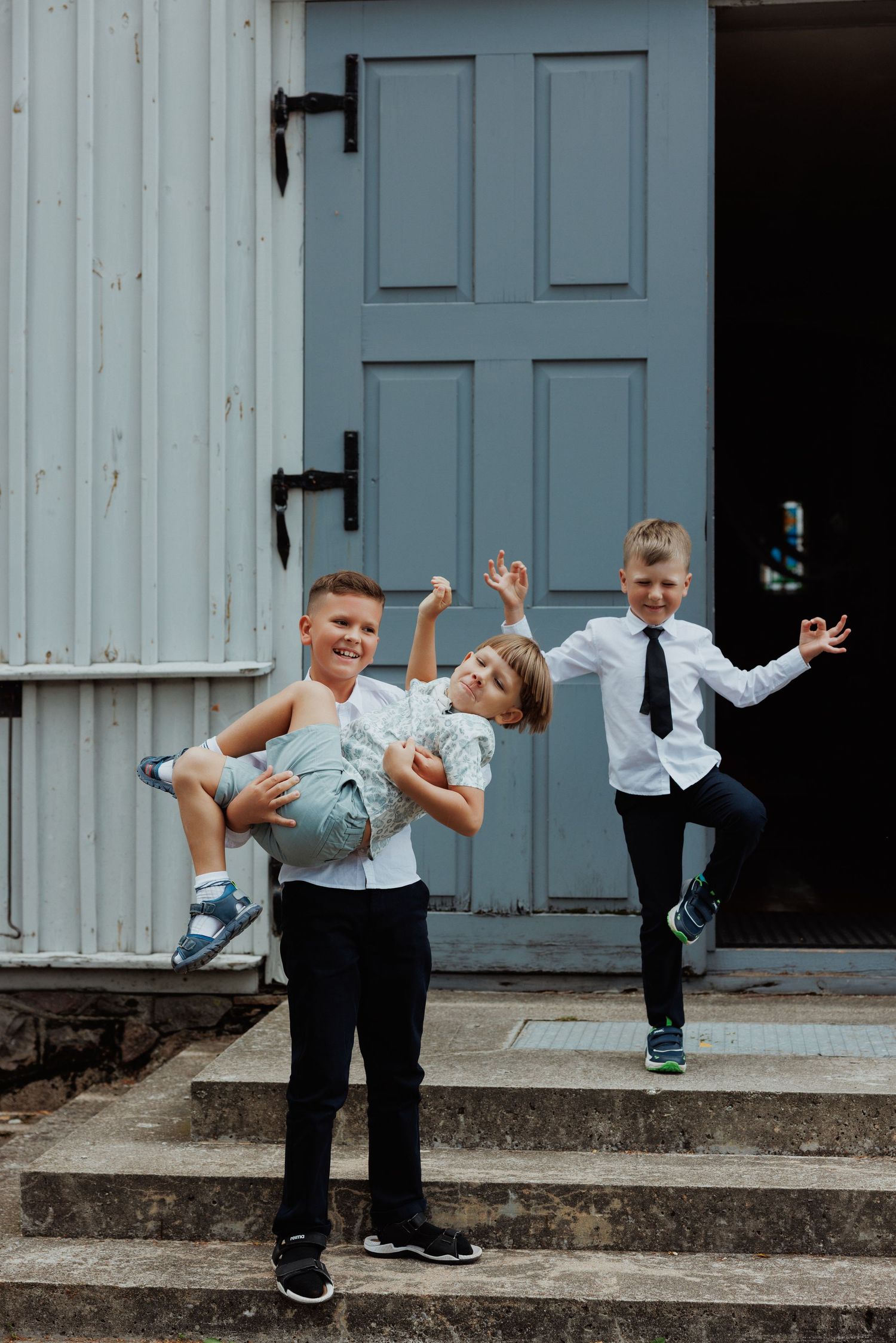 Three children in formal attire playing and posing playfully on stone steps in front of a blue door.