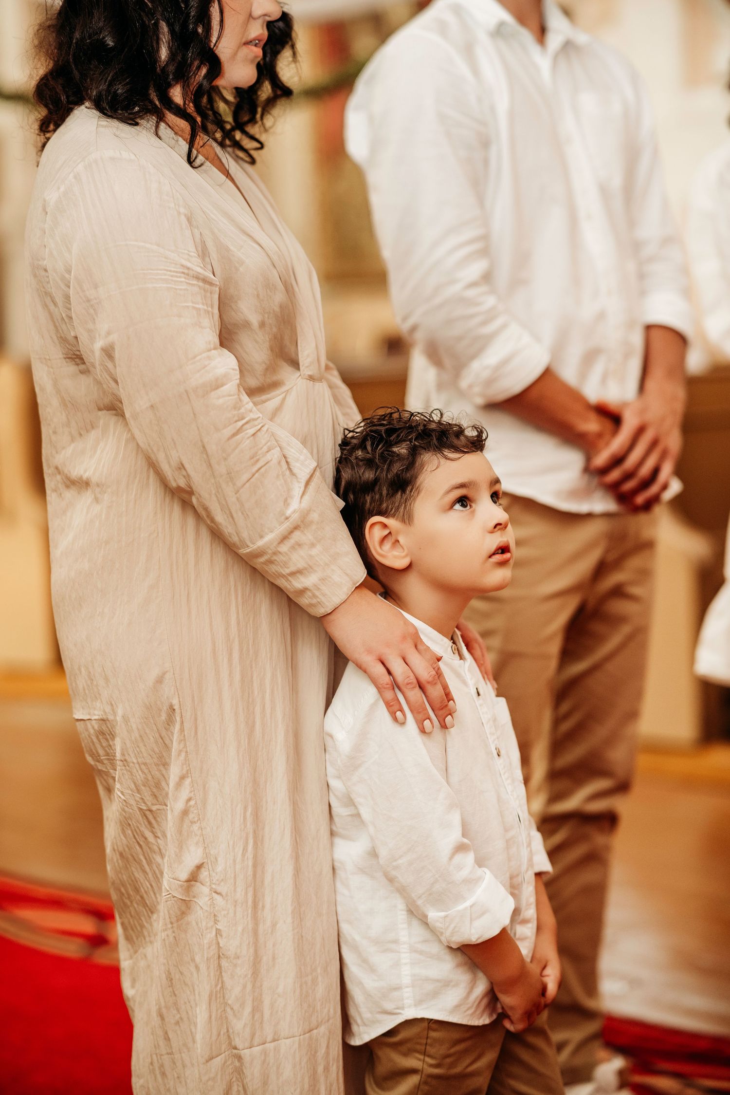 A young boy in a white shirt stands with family members during what appears to be a formal gathering or ceremony.