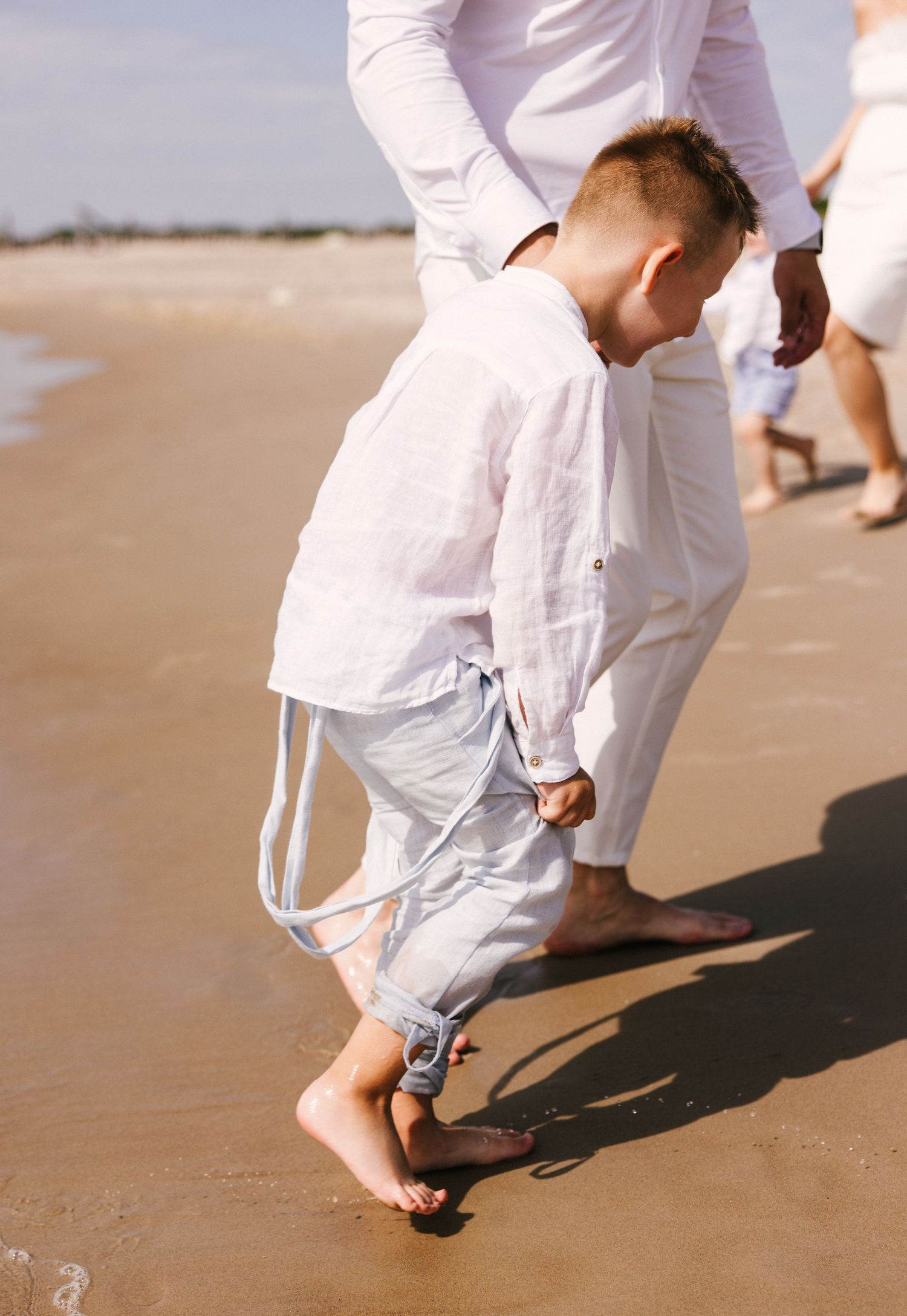 Close-up of feet walking on wet beach sand in white clothing.