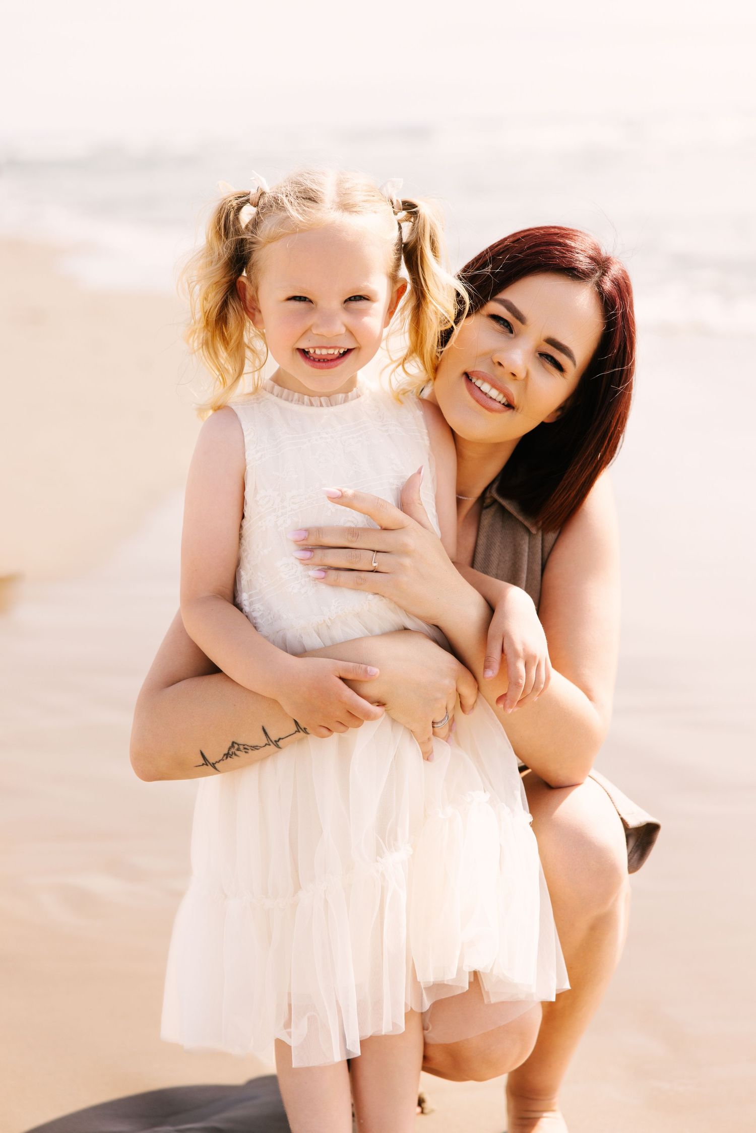 Mother and daughter in white dresses sharing joyful moments on sunny beach.