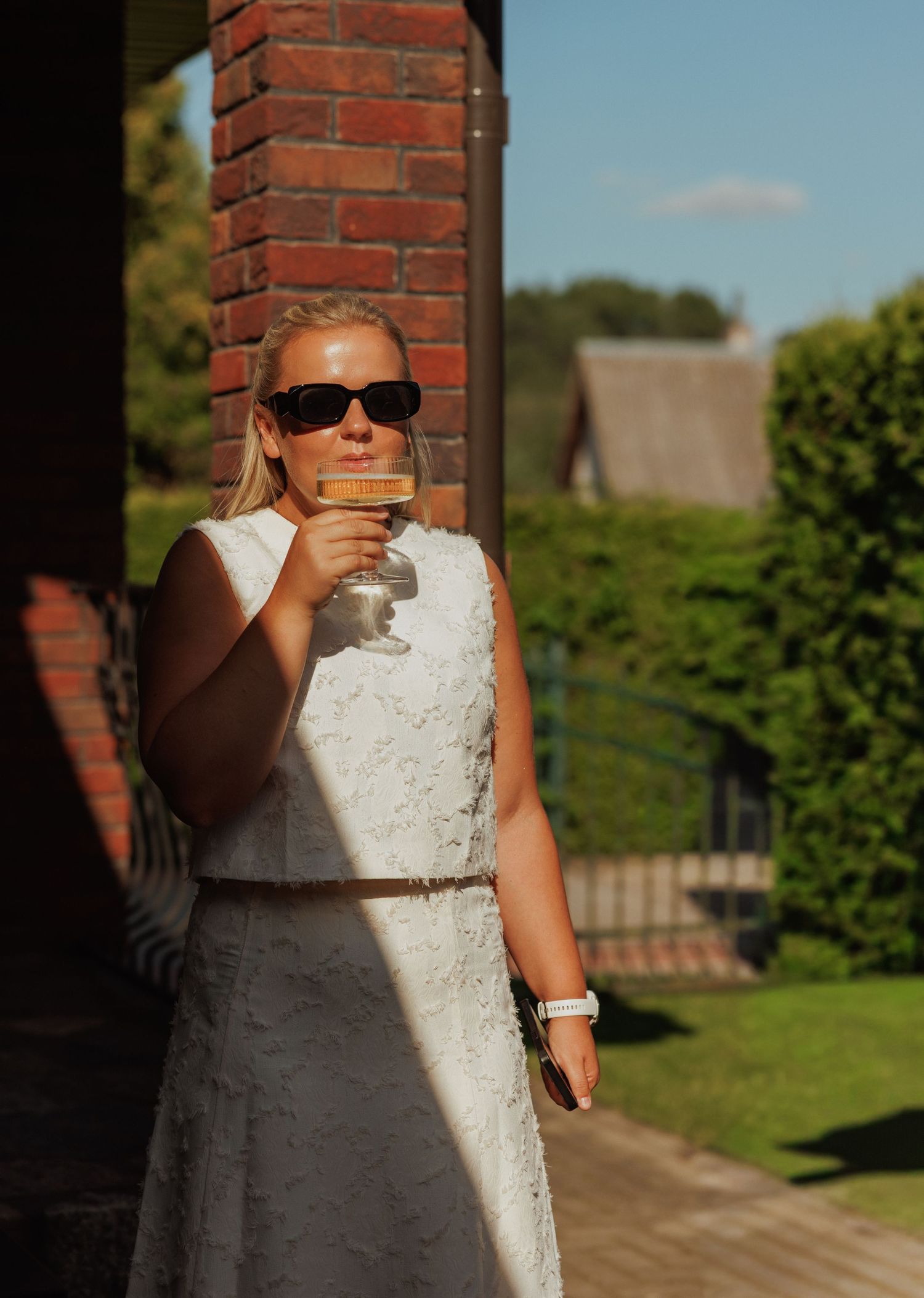 Person in a white dress standing against a brick wall in natural sunlight.