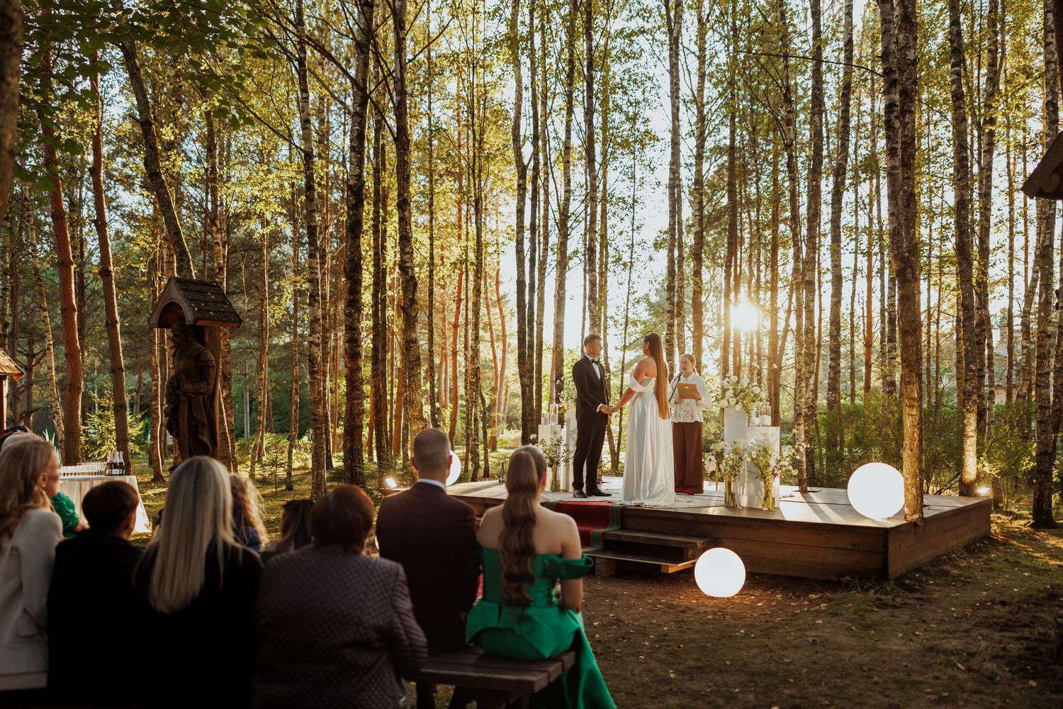 Wide panoramic view of a forest wedding ceremony setting with tall pine trees and golden sunlight.