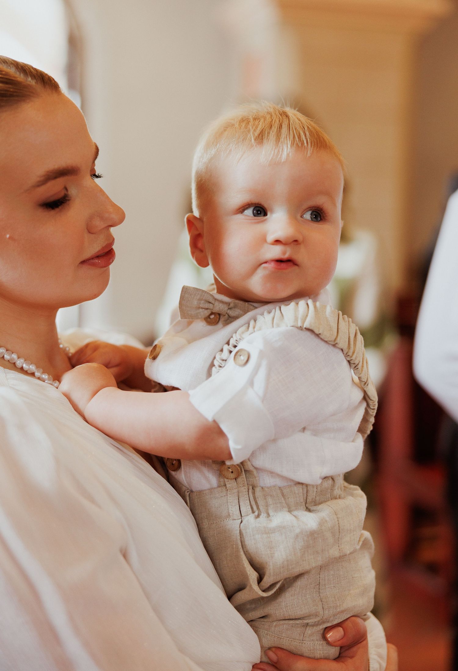 A tender moment captured between parent and baby in white clothing against a warm indoor setting.