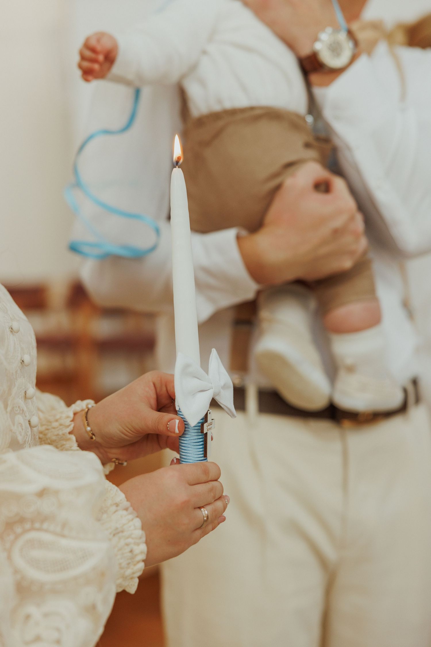 Hands holding white candles during a religious ceremony with delicate lace details visible in the background.