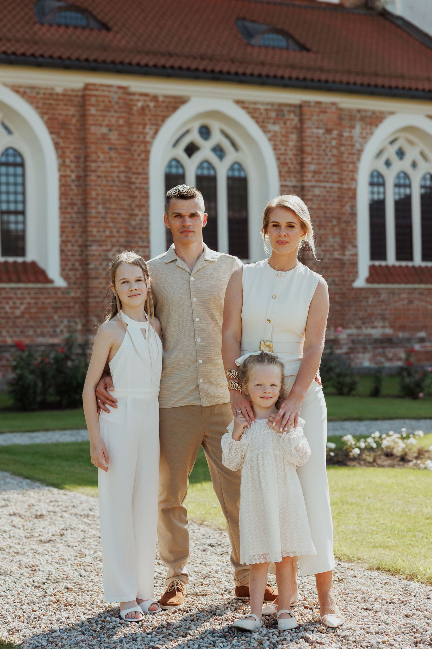 Family in coordinated cream and beige outfits poses together outside a brick church building.