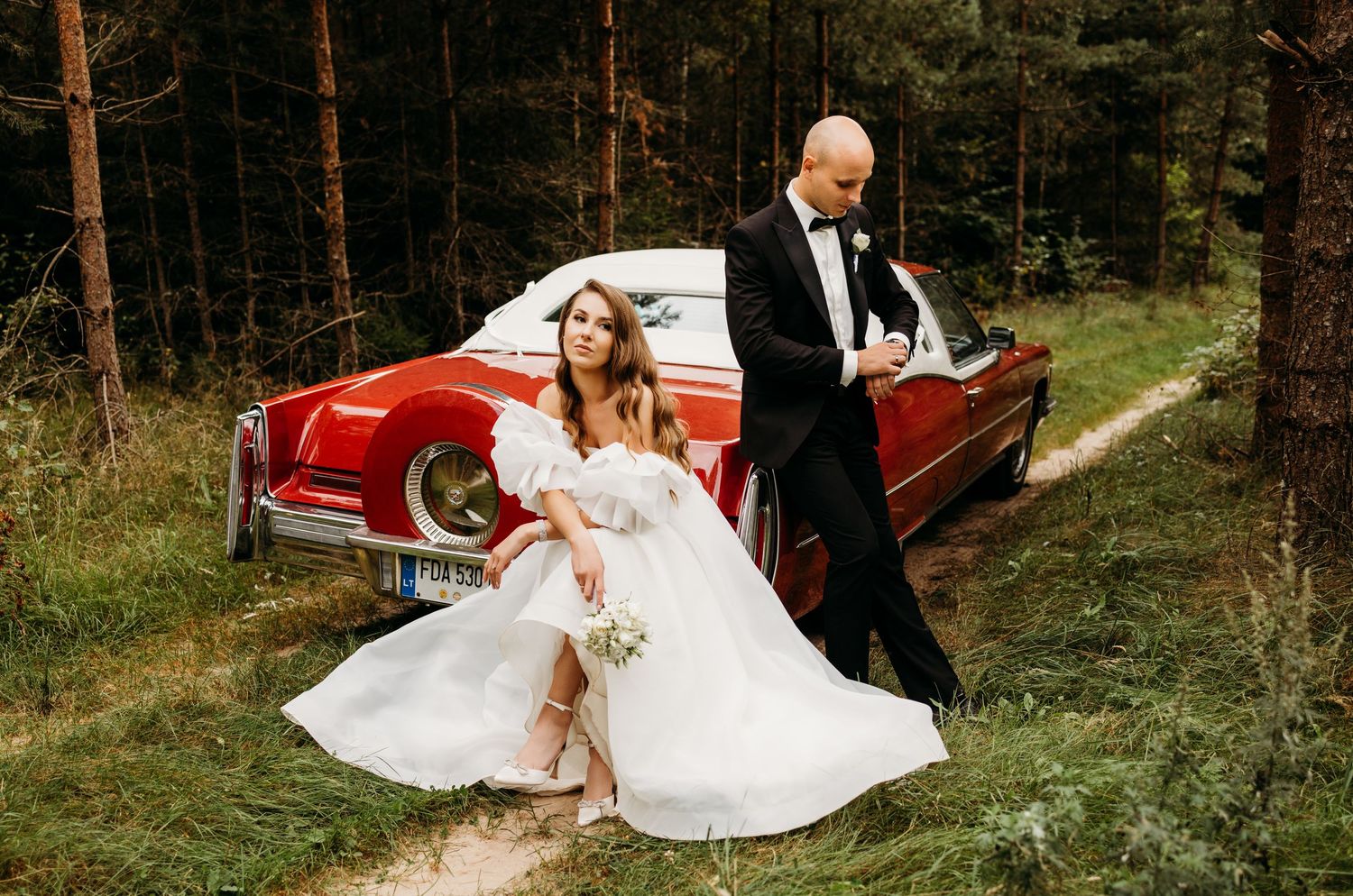 Wedding photography series in forest setting with vintage red car and pine trees.
