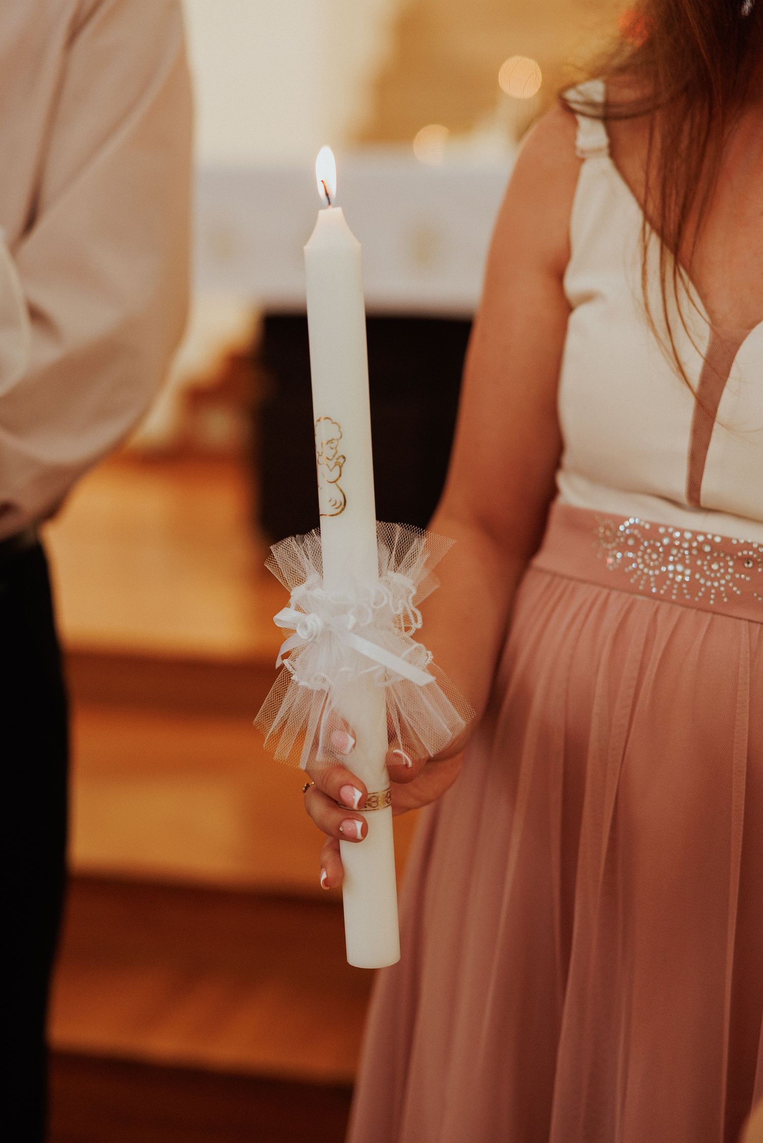 White decorated baptism or christening candles with tulle bows held against blush pink dresses.
