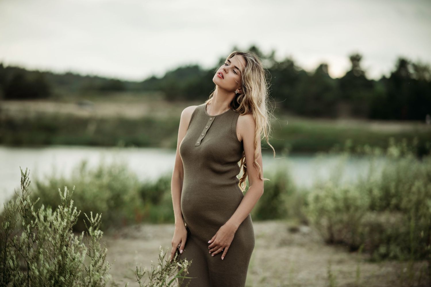 Maternity photoshoot by a lake featuring an olive green dress against a natural outdoor backdrop.