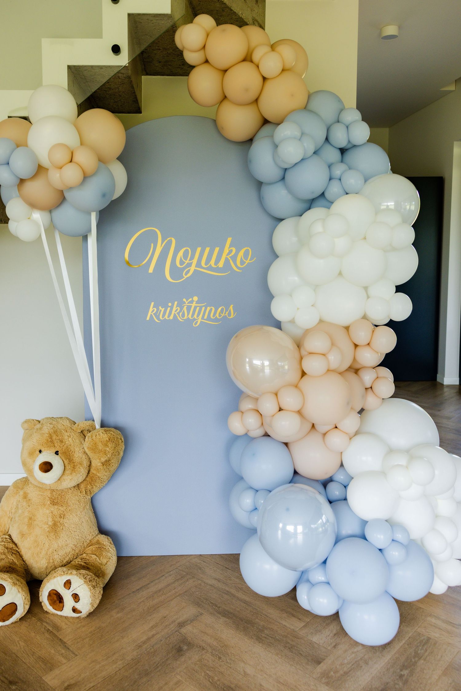 Baby shower backdrop with balloon arch in blue, peach and white with teddy bear decoration.
