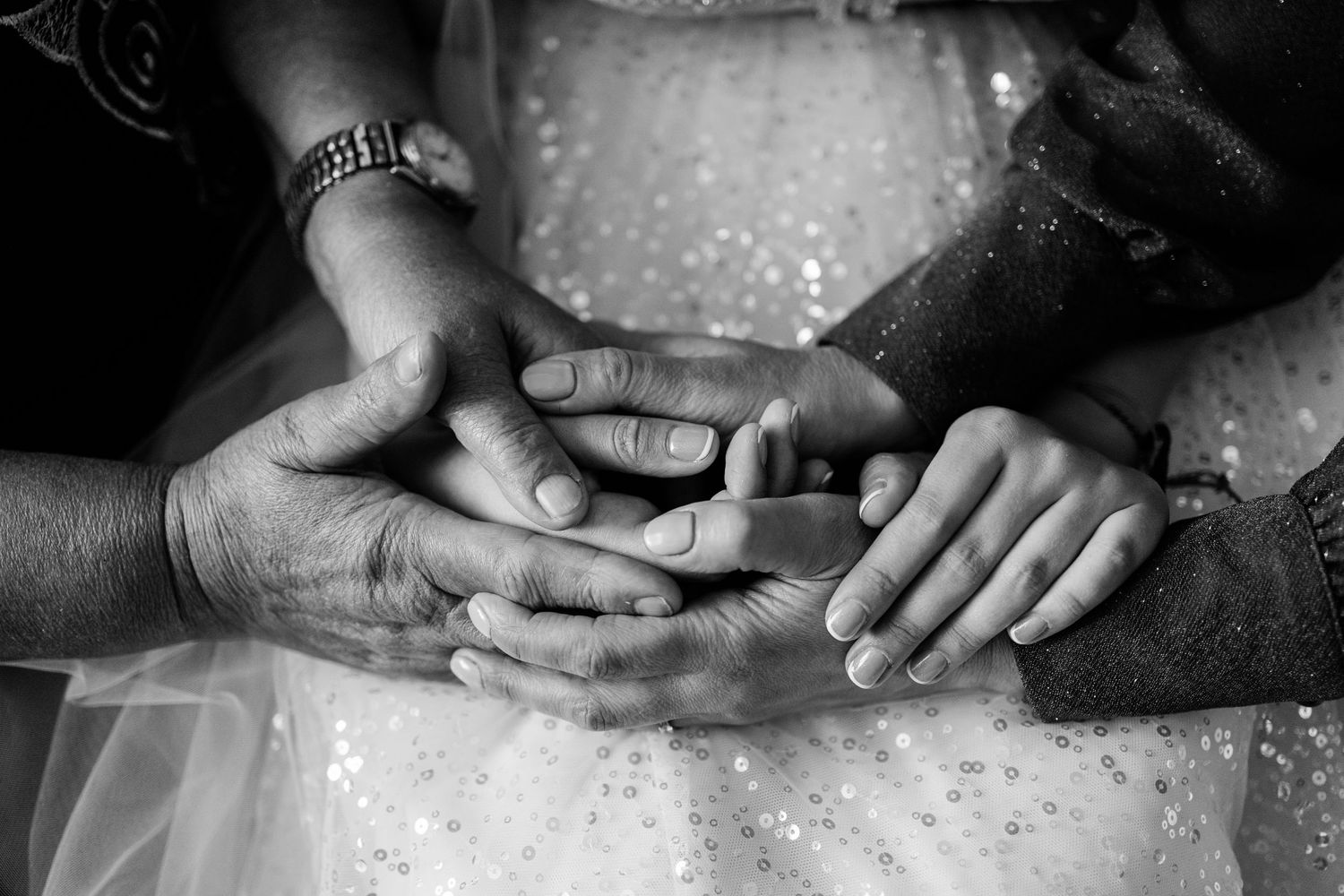 Black and white close-up of hands clasped together over a sparkly white dress fabric.