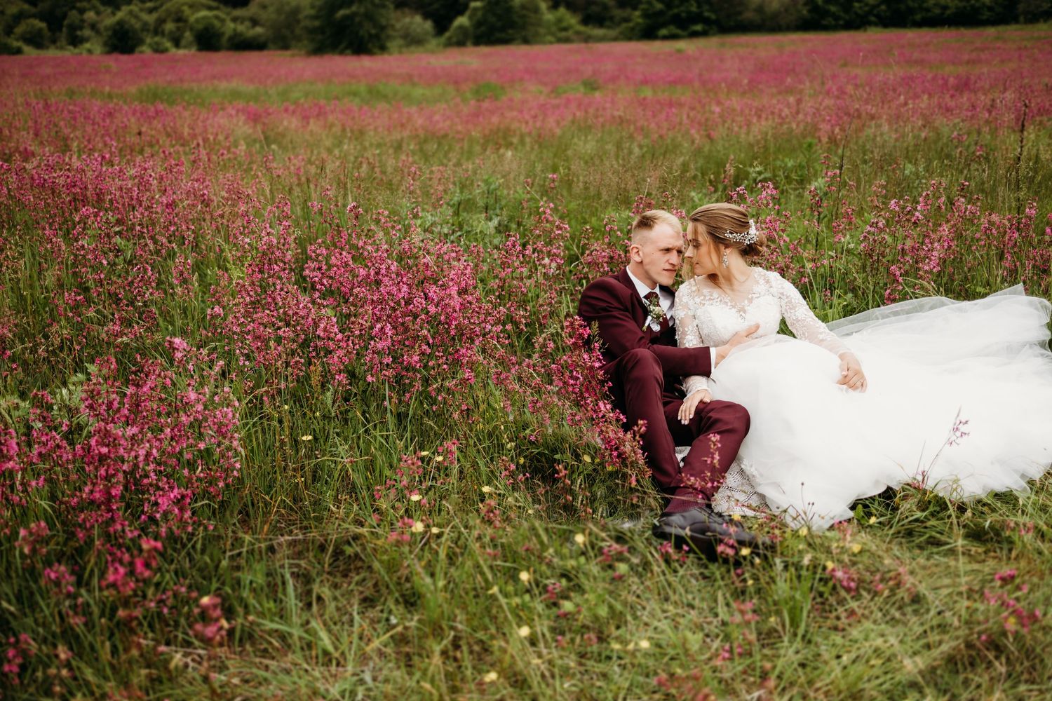A joyful wedding couple sitting together in a field of pink wildflowers.