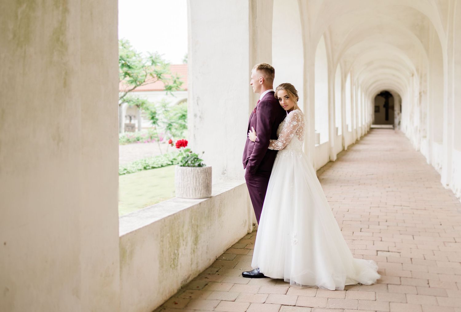 Elegant wedding couple shares tender moments in white arched hallway.