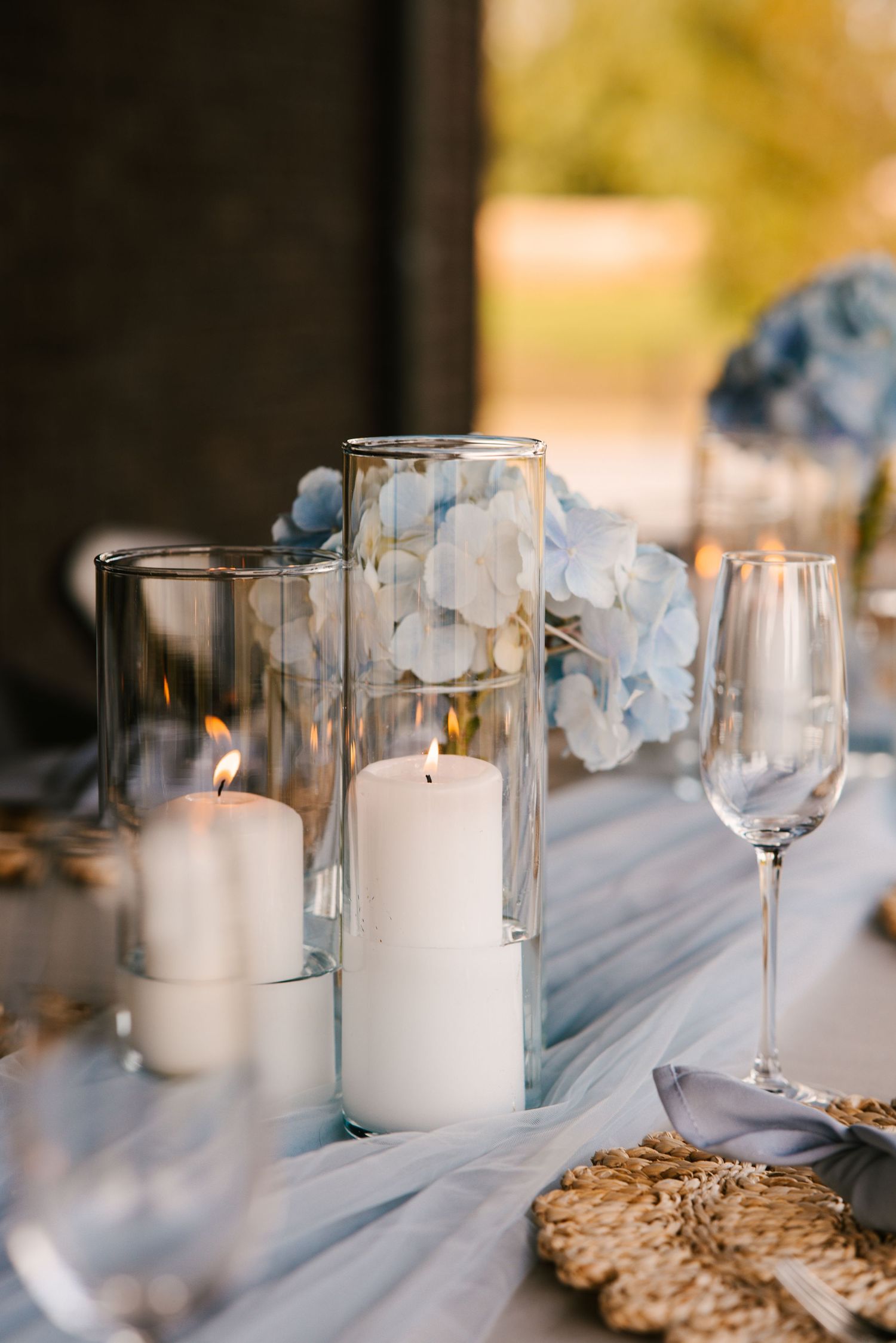 White pillar candles and blue floral centerpieces line a formal dining table with delicate glassware.