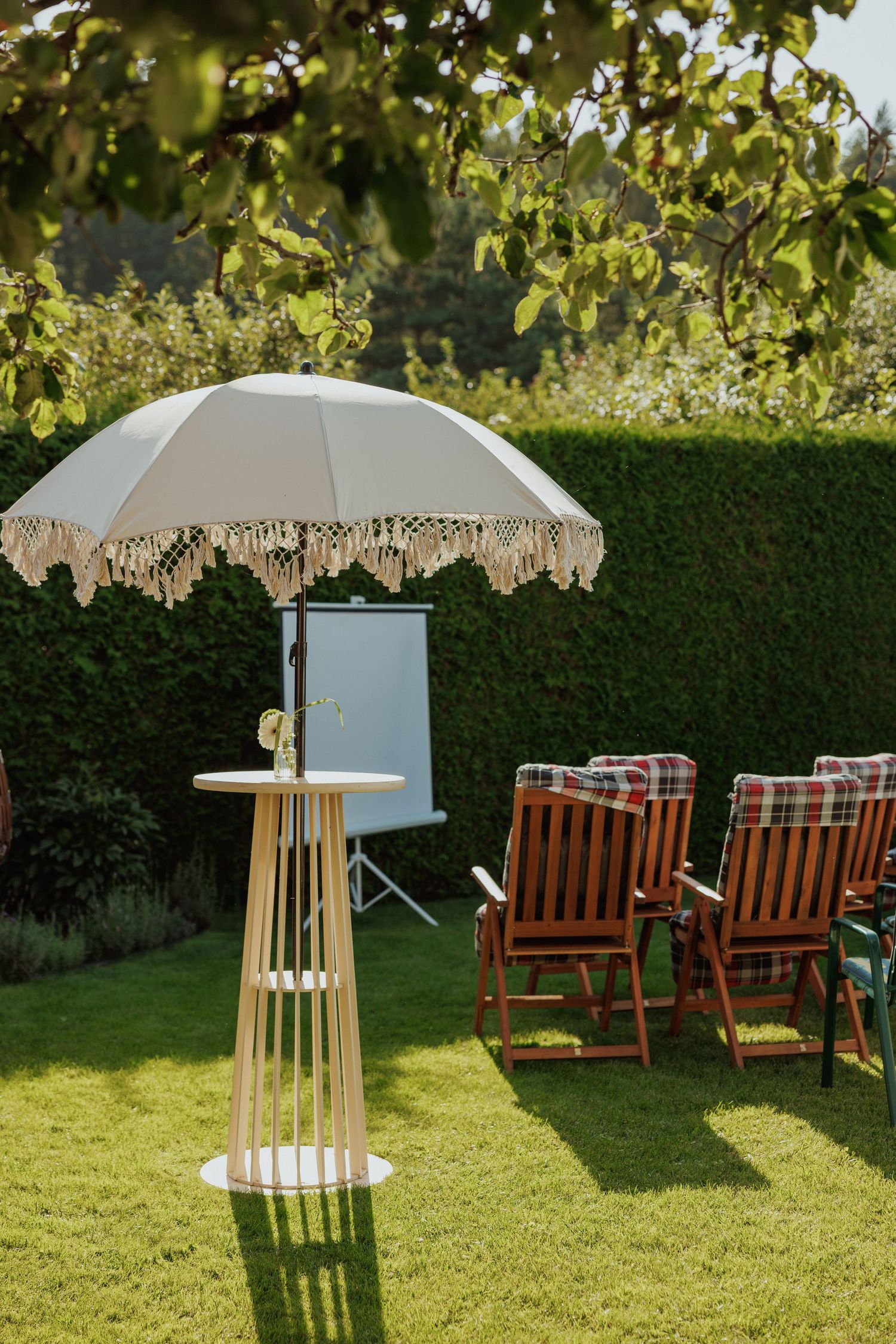 White fringed umbrella and wooden deck chairs set up on manicured lawn for outdoor event.