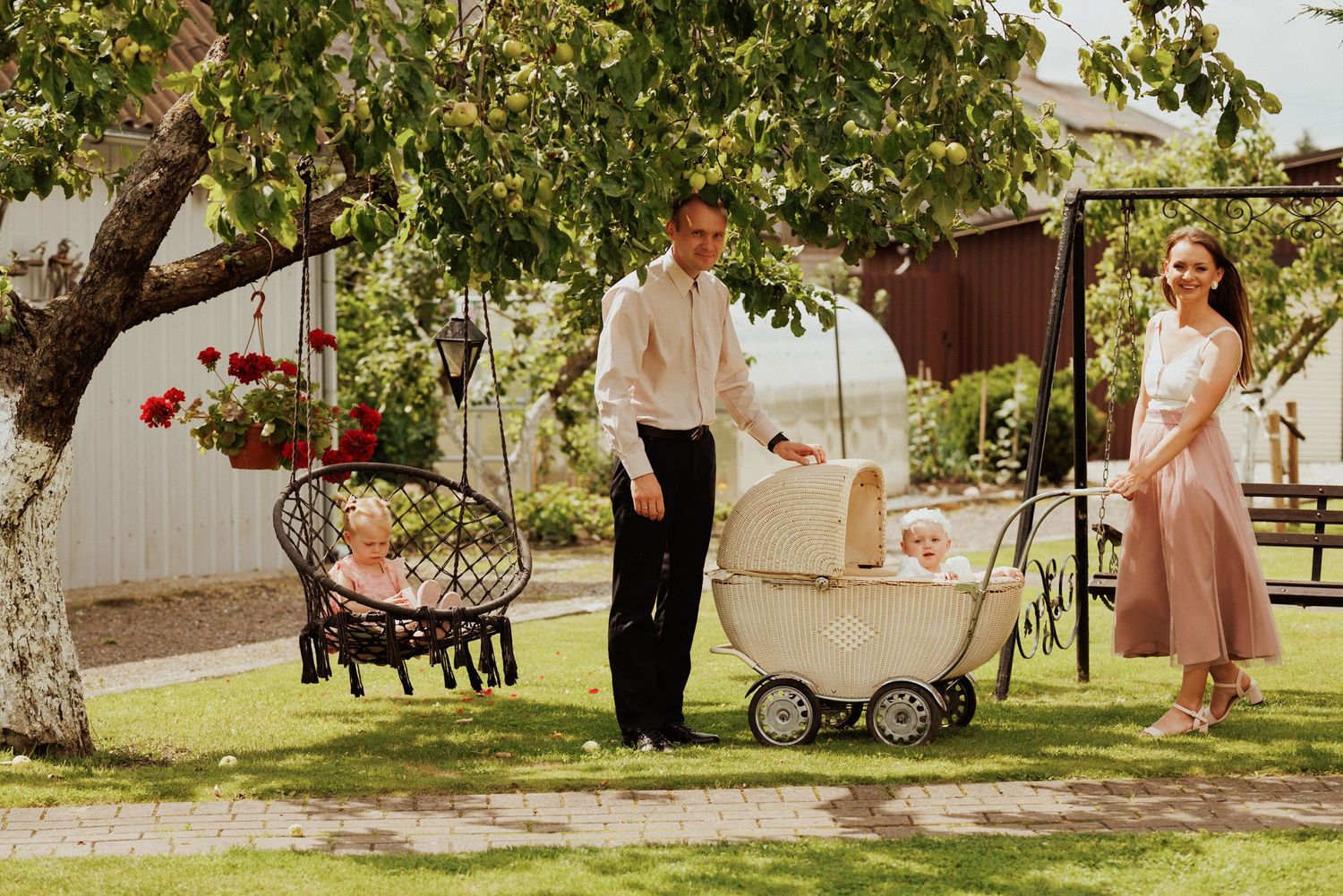 Wedding party walking through a lush garden setting with trees and strollers visible.