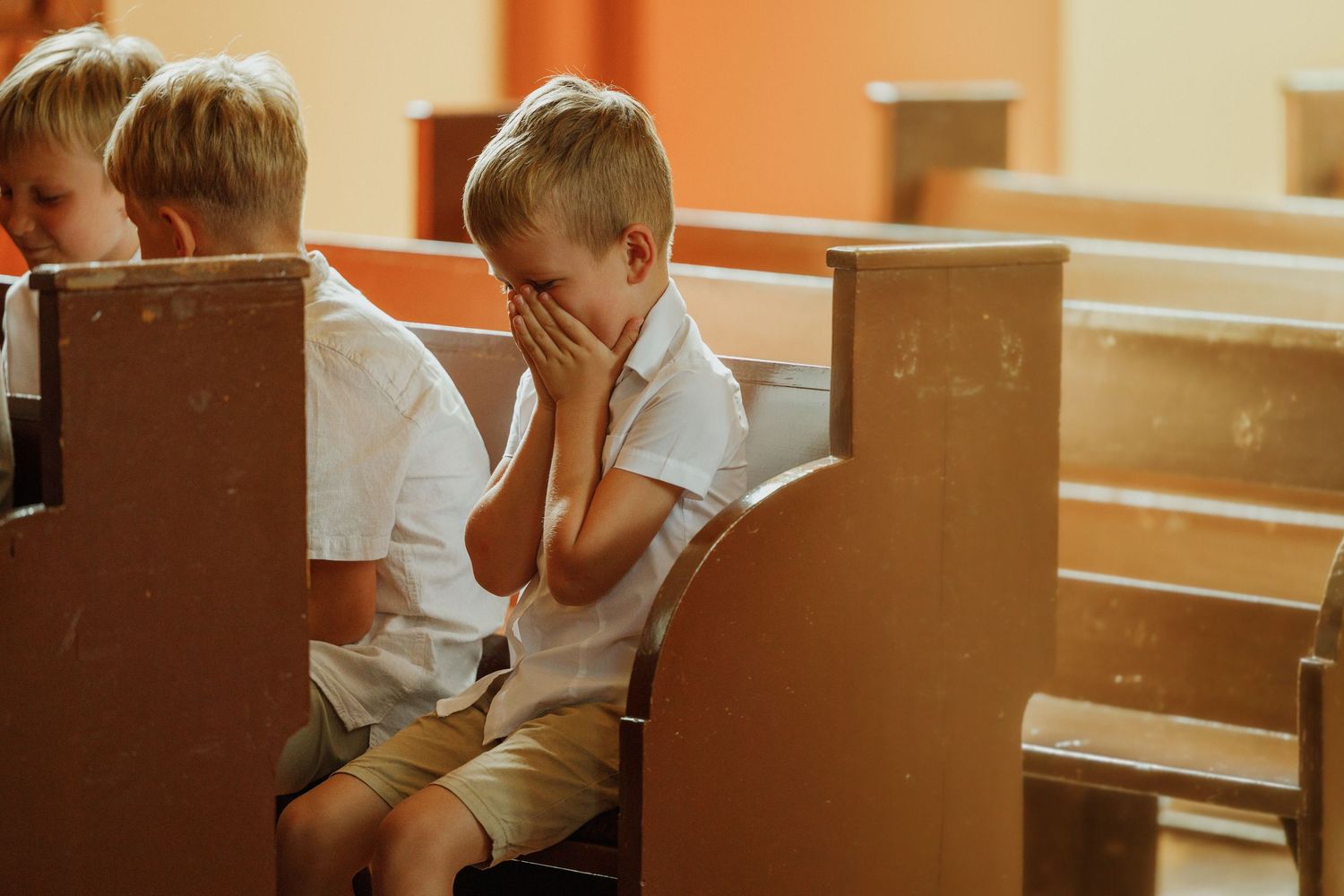 A student sits at a wooden desk in a classroom, resting their head on their hand while appearing to be deep in thought.