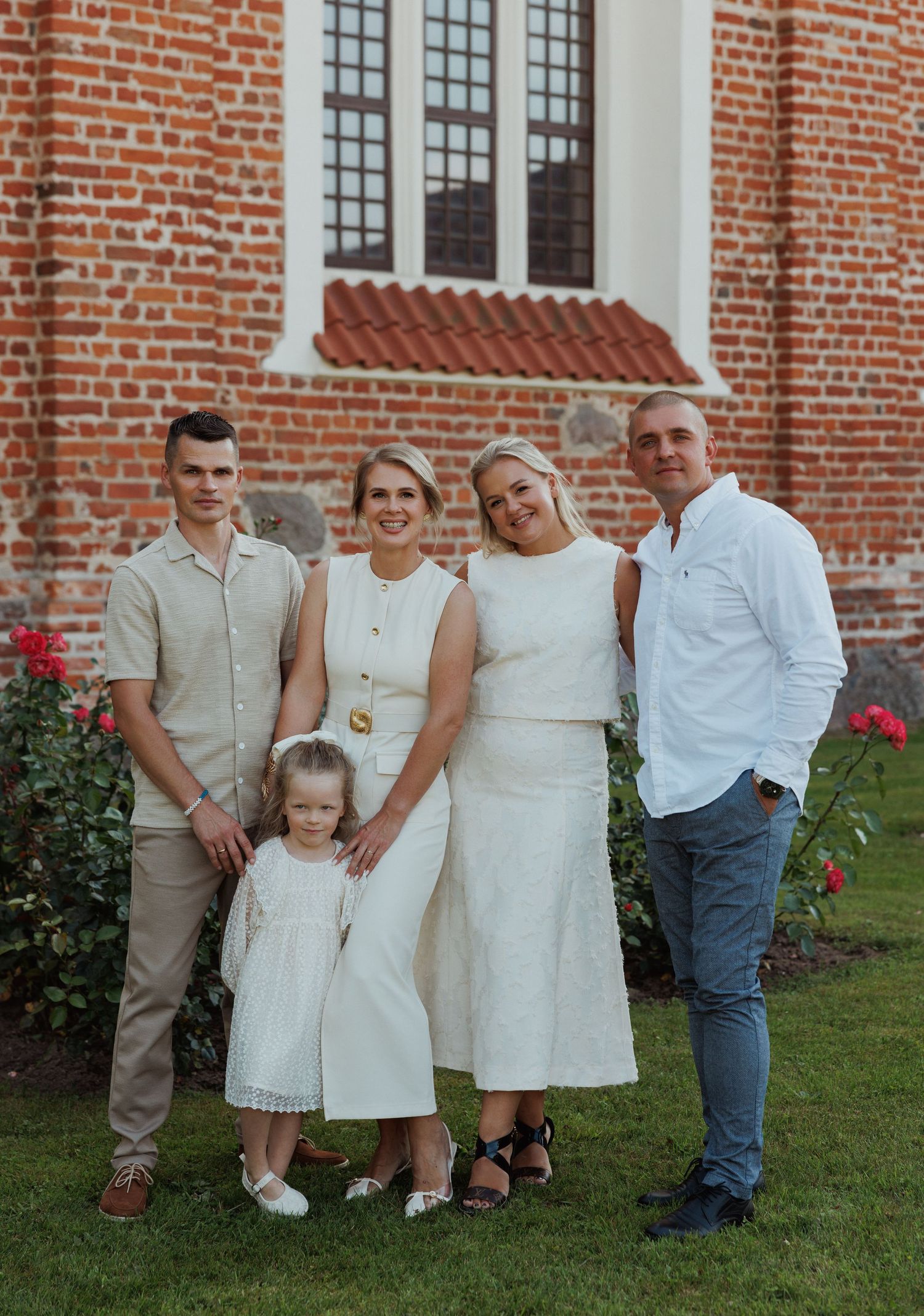 A group in coordinating white and beige outfits poses together in front of a brick church building.