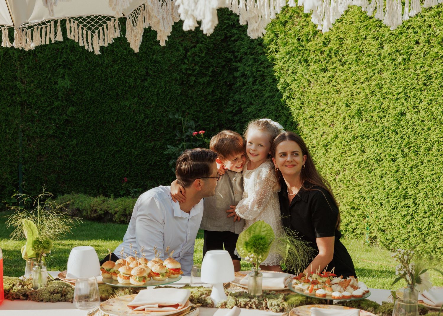 Garden party scene with white tent and guests gathered around decorated tables.