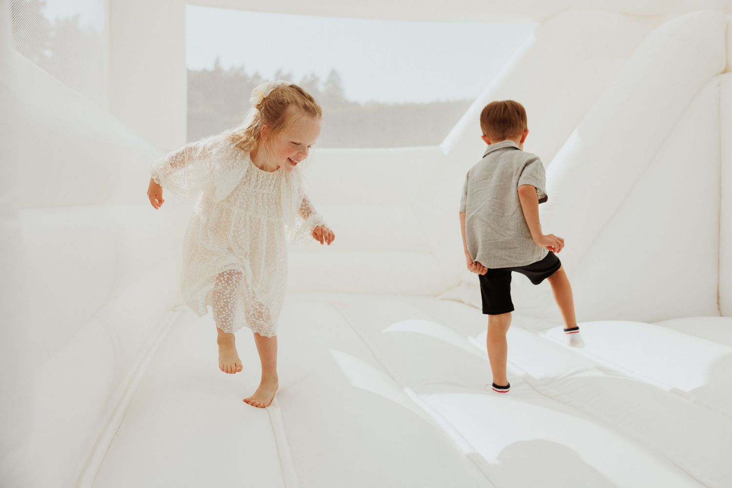 Children playing and running on white furniture in a bright indoor setting.