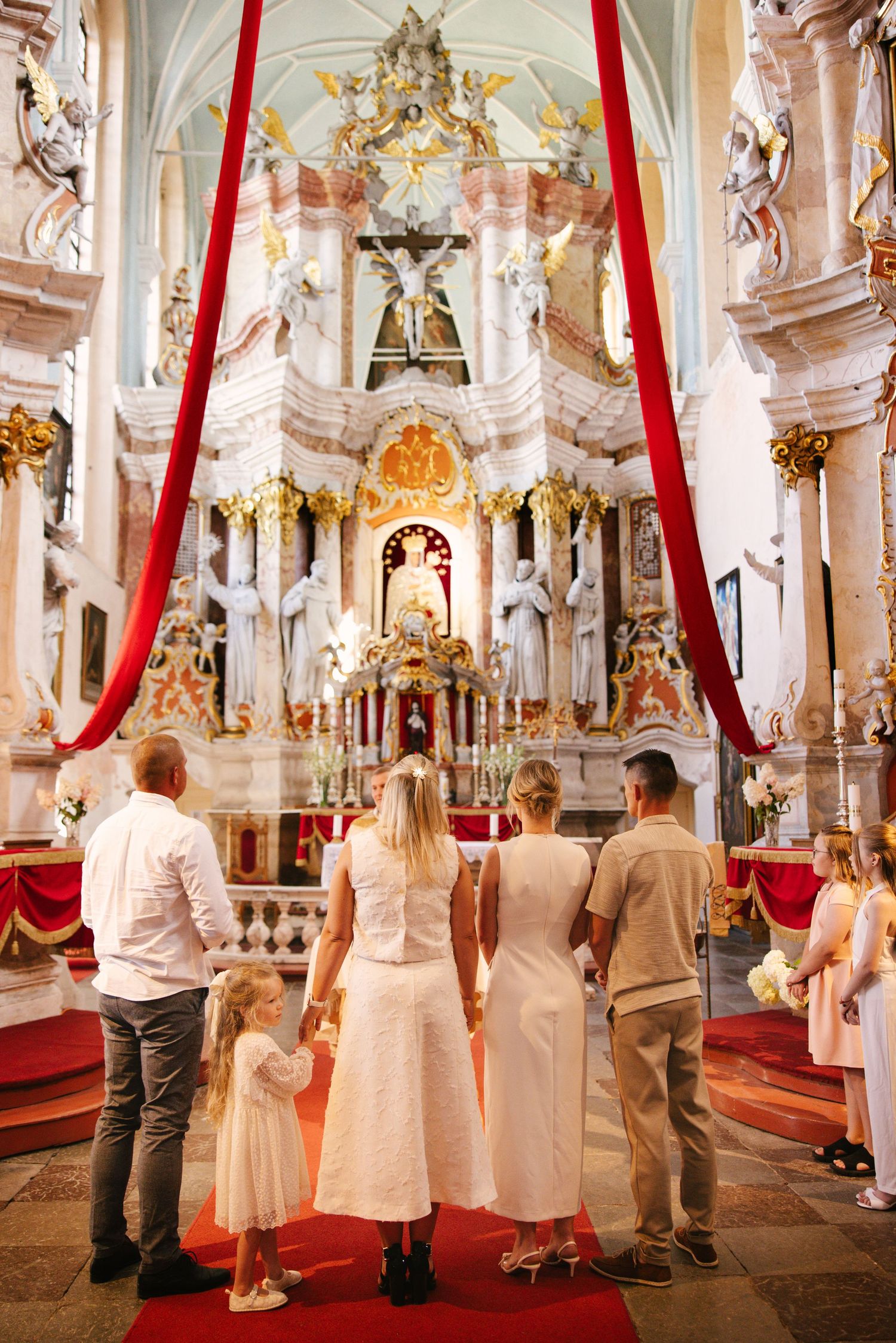 Elegant church interior with red curtains and ornate baroque decor during a wedding ceremony.