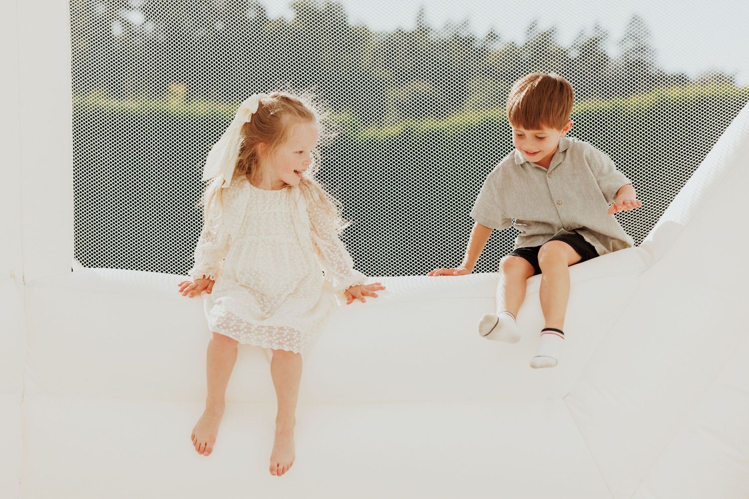 Playful family photoshoot with white dresses and casual attire in natural outdoor setting.