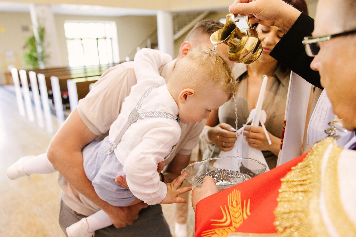 A young child in formal attire bends over to kiss a religious object during a church ceremony.