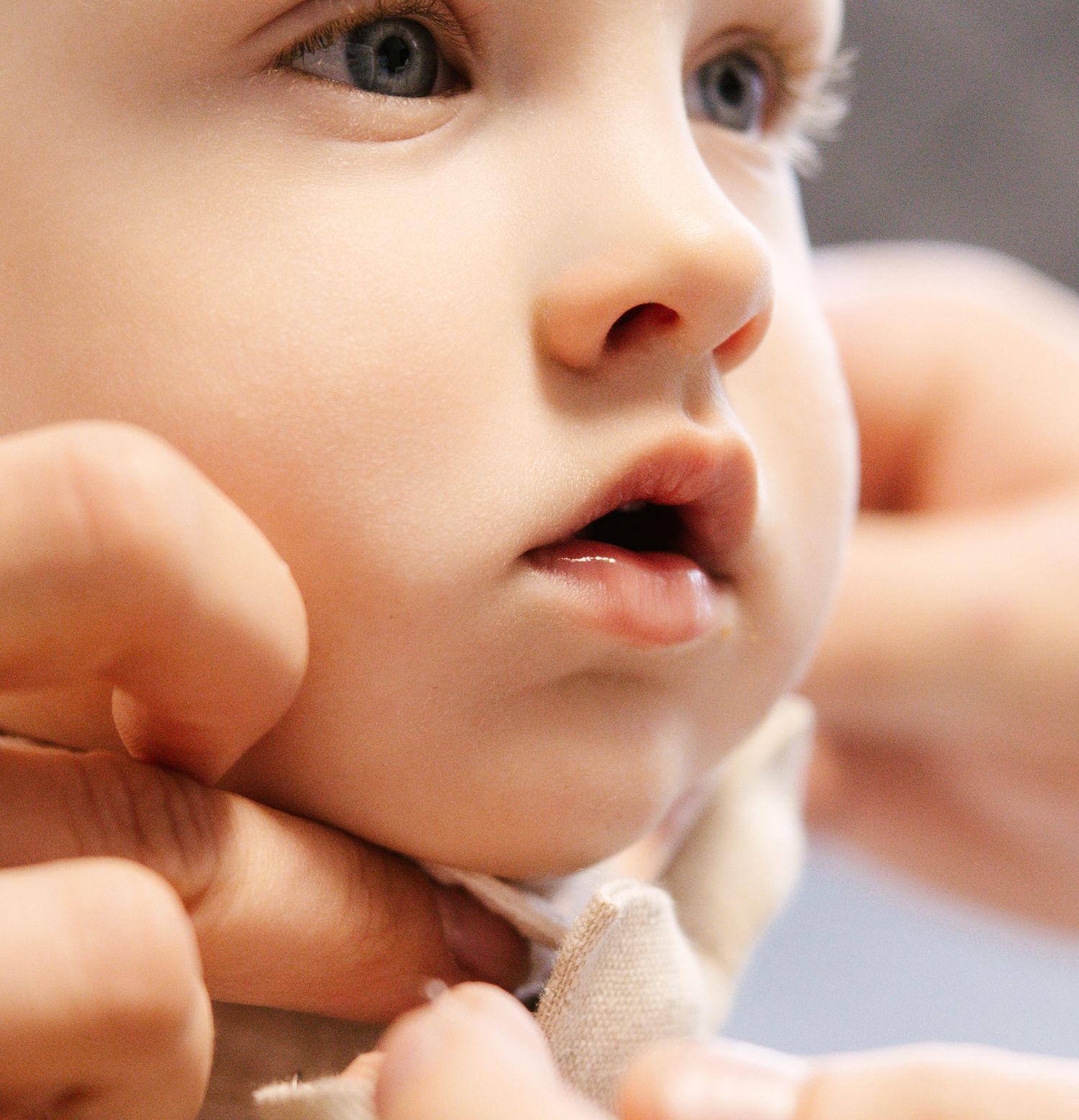 Close-up shot of a baby's face being gently touched by an adult hand.