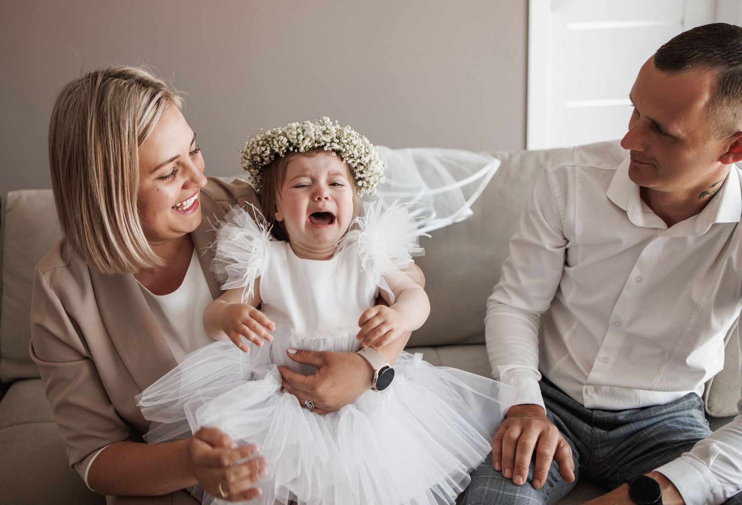 Family wearing white clothing shares joyful moments together on a couch during an indoor photo session.