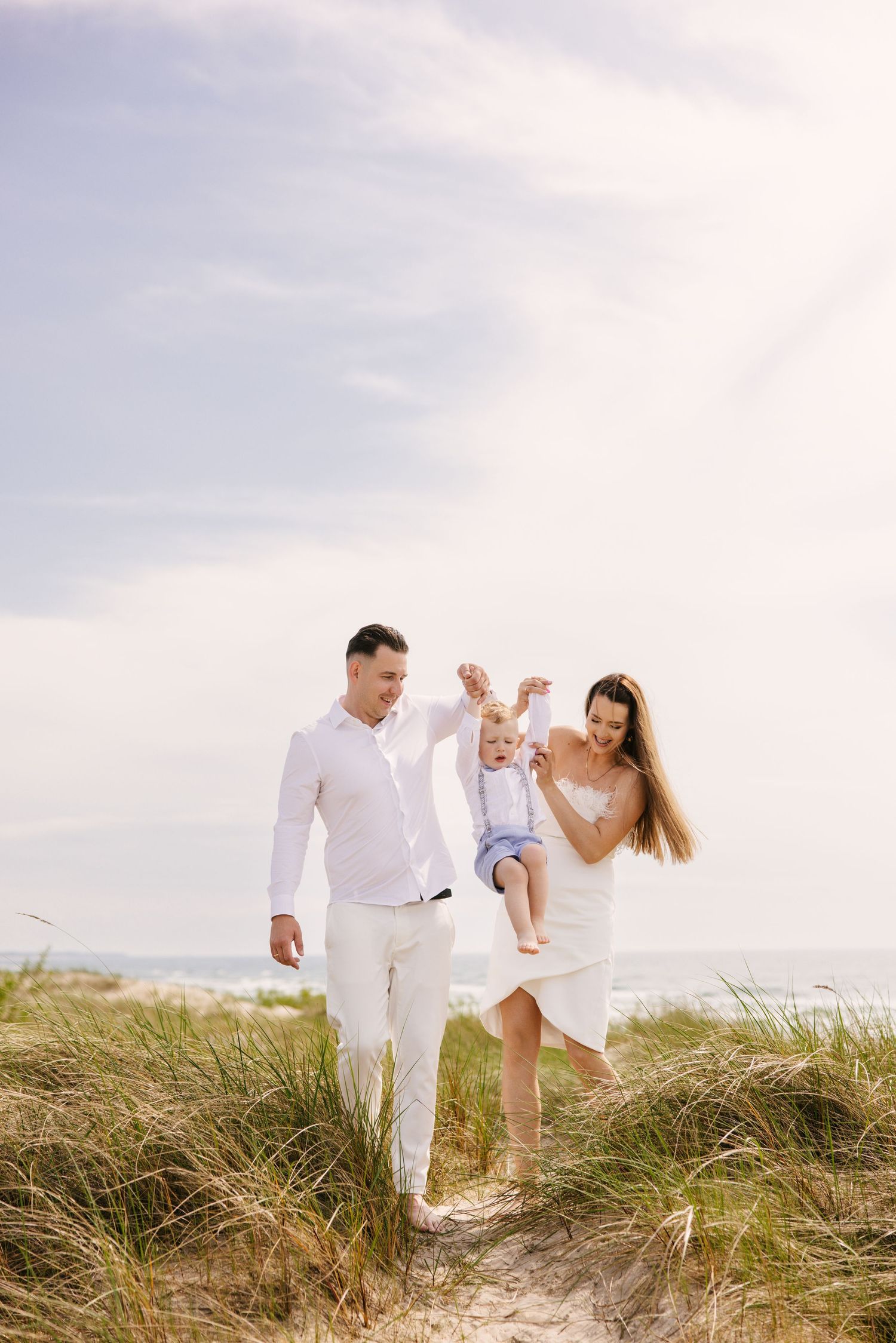 Family walking together through coastal grass on sunny beach day.