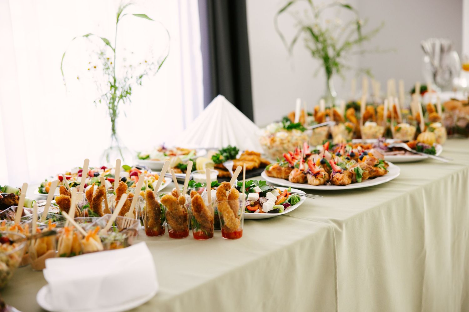 Long buffet table with appetizers and hors d'oeuvres arranged on white tablecloth.
