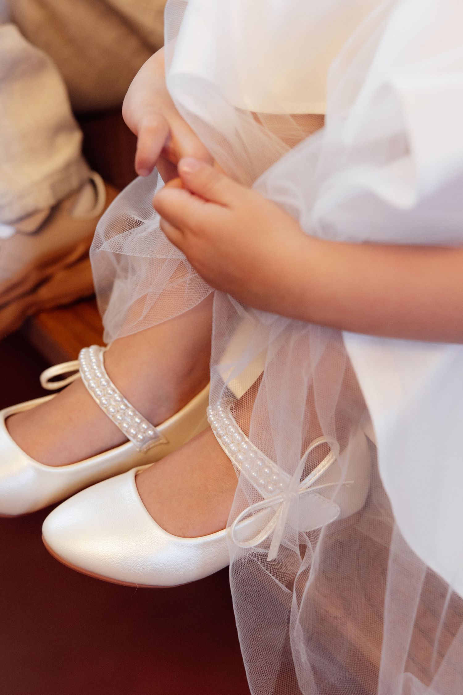 Close-up of a young girl in a white tulle dress wearing elegant satin pearl-embellished ballet flat shoes.